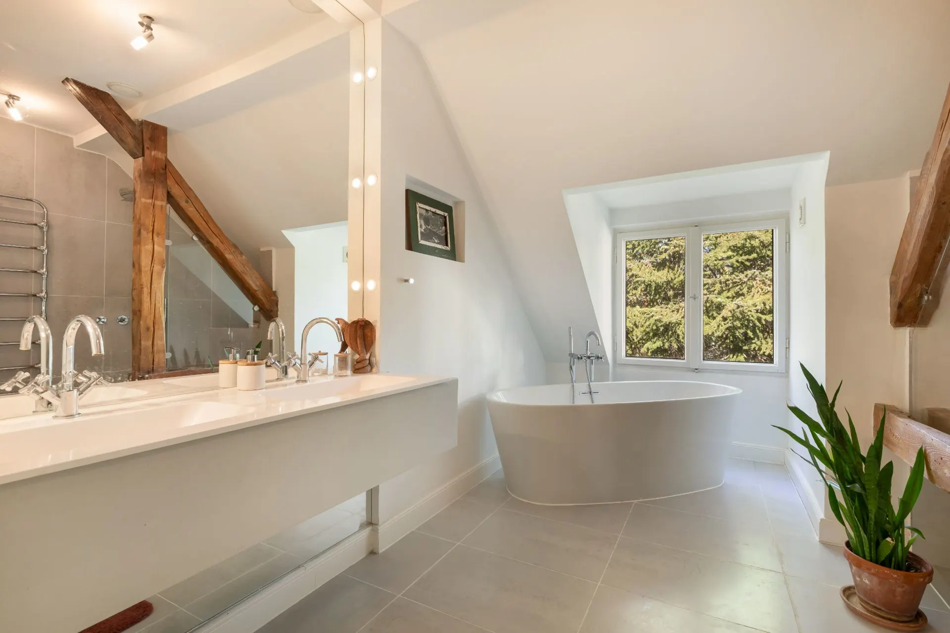 Modernes Badezimmer mit freistehender Badewanne, großem Spiegel, Pflanze und Holzdetails.