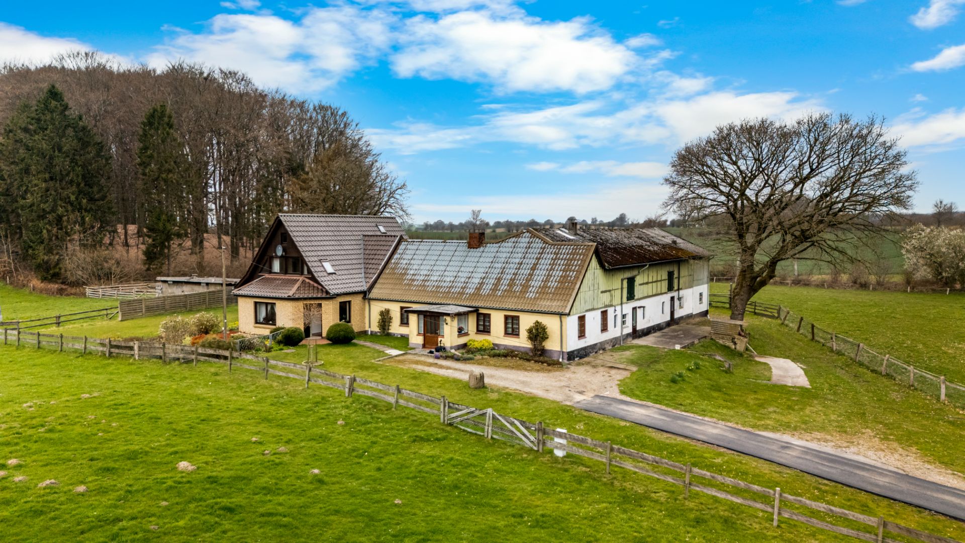 Großes Bauernhaus mit eingezäuntem Garten und Baum auf einer grünen Wiese.