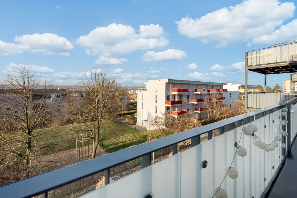 Blick von einem Balkon auf einen Garten und ein modernes Wohngebäude mit roten Balkonen.