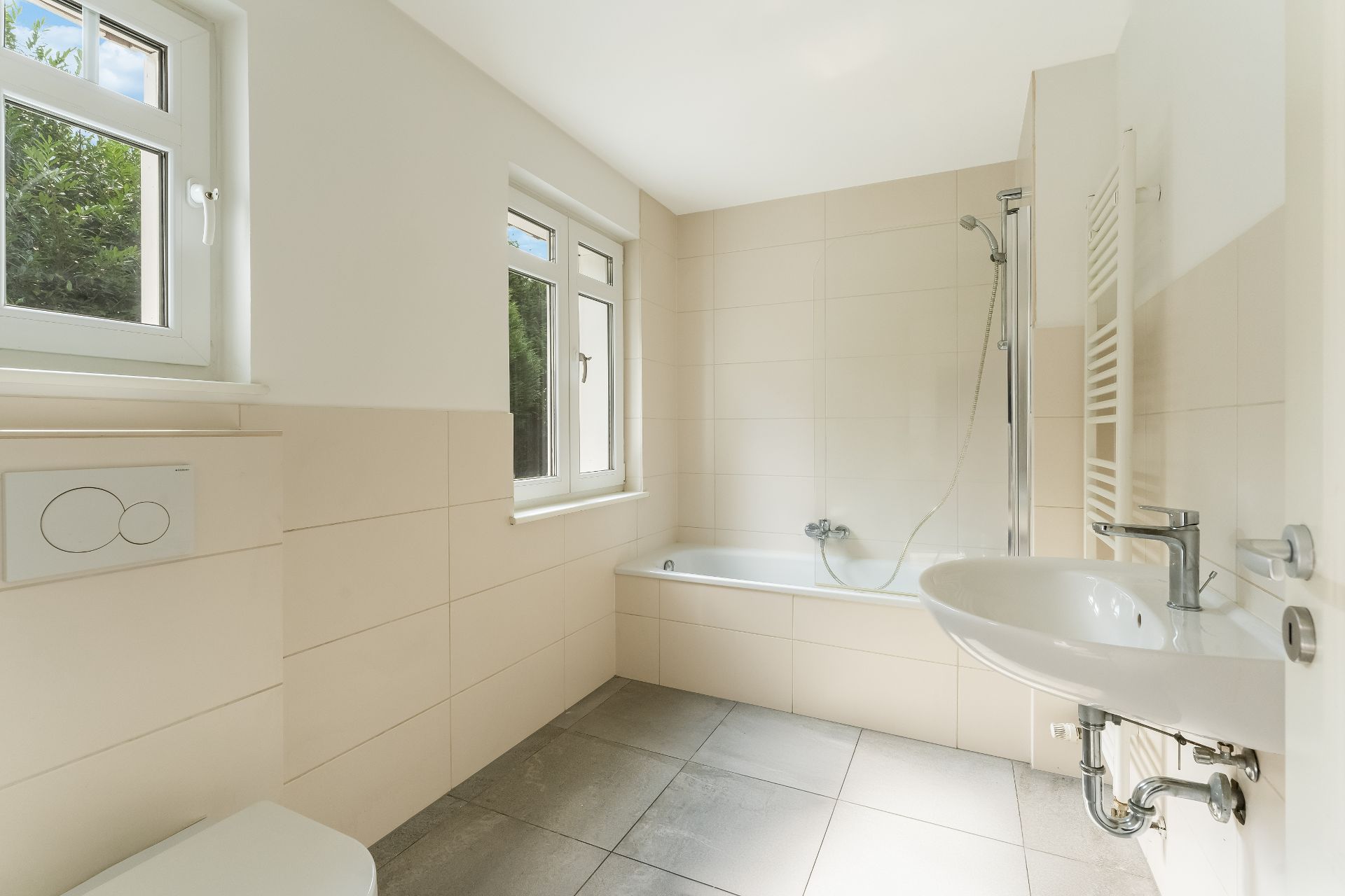 Helles Badezimmer mit Badewanne, Waschbecken, WC und zwei Fenstern.
