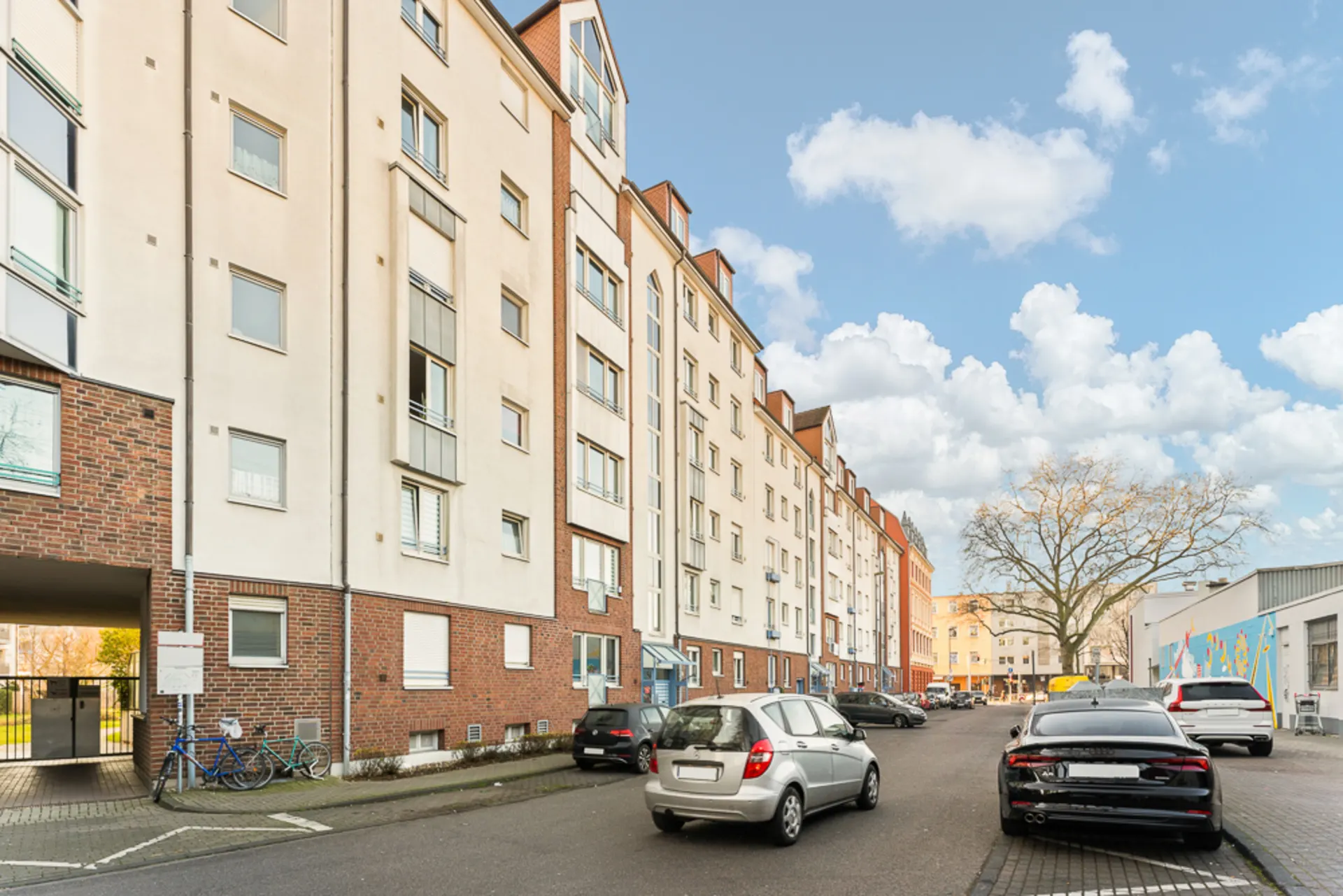 Mehrstöckiges Wohnhaus mit geparkten Autos und Fahrrädern an der Straße.