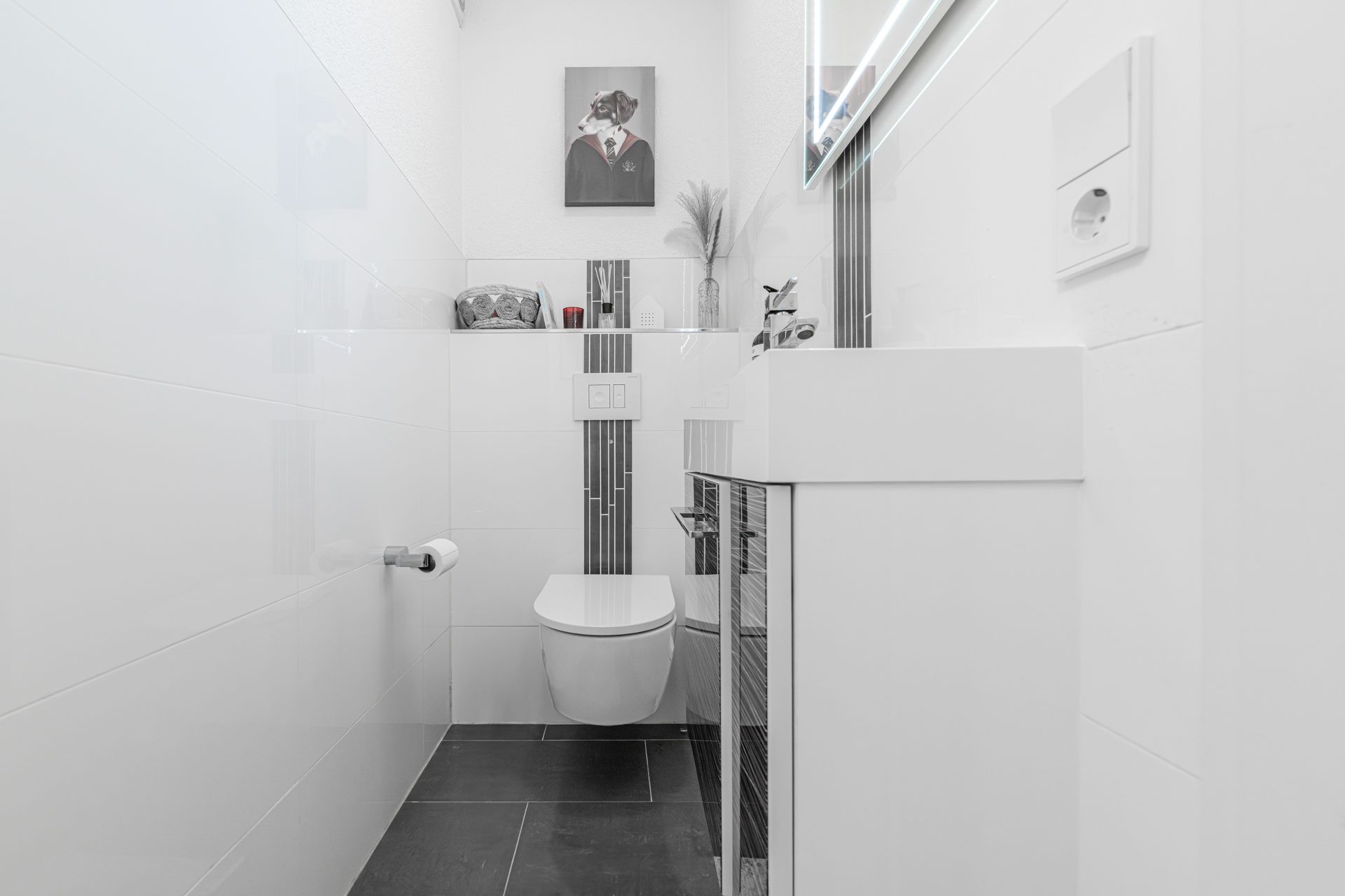 Modernes, weiß gefliestes Gäste-WC mit Wandtoilette, Waschbecken und Wandbild eines Hundes.