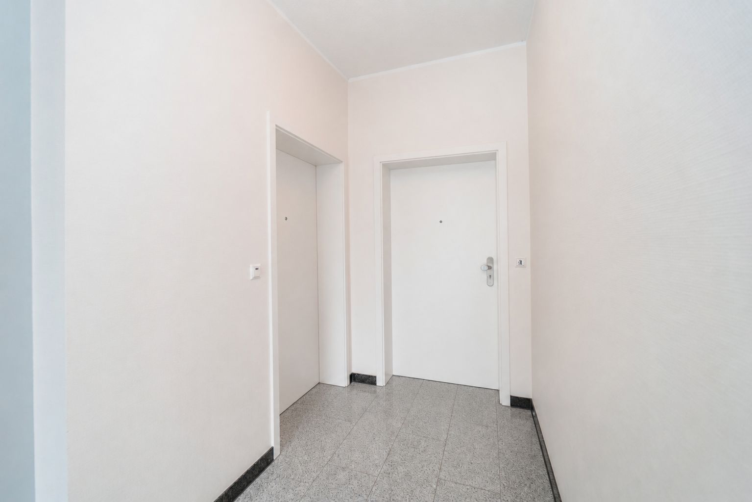 Heller Flur mit zwei weißen Türen und grauem Fliesenboden.