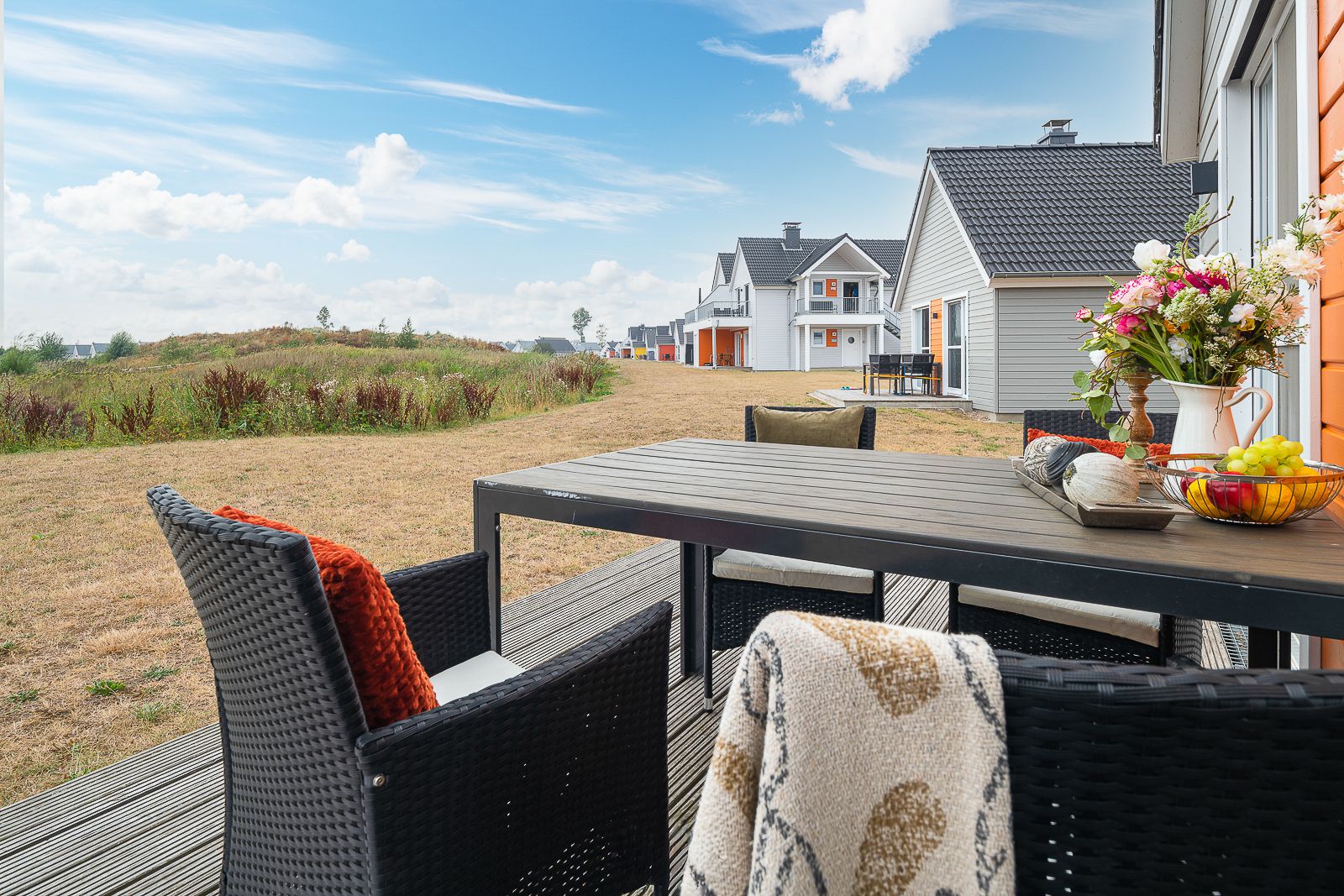 Terrasse mit Tisch, vier Stühlen und Blumenvase, Blick auf weitere Wohnhäuser und Wiese.
