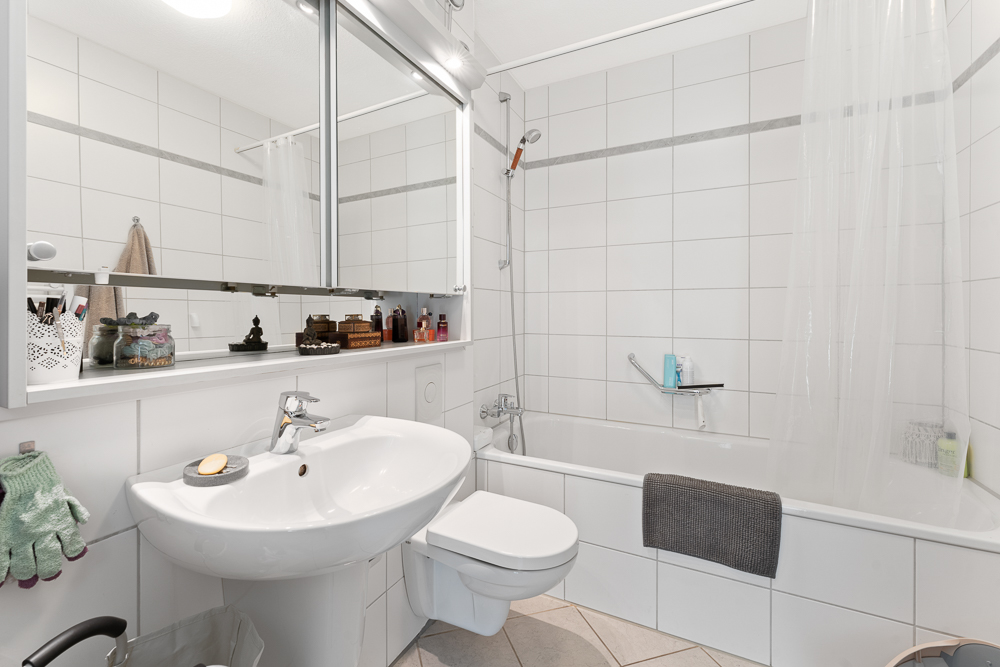 Modernes Badezimmer mit weiß gefliester Badewanne, Waschbecken, Spiegel und WC.