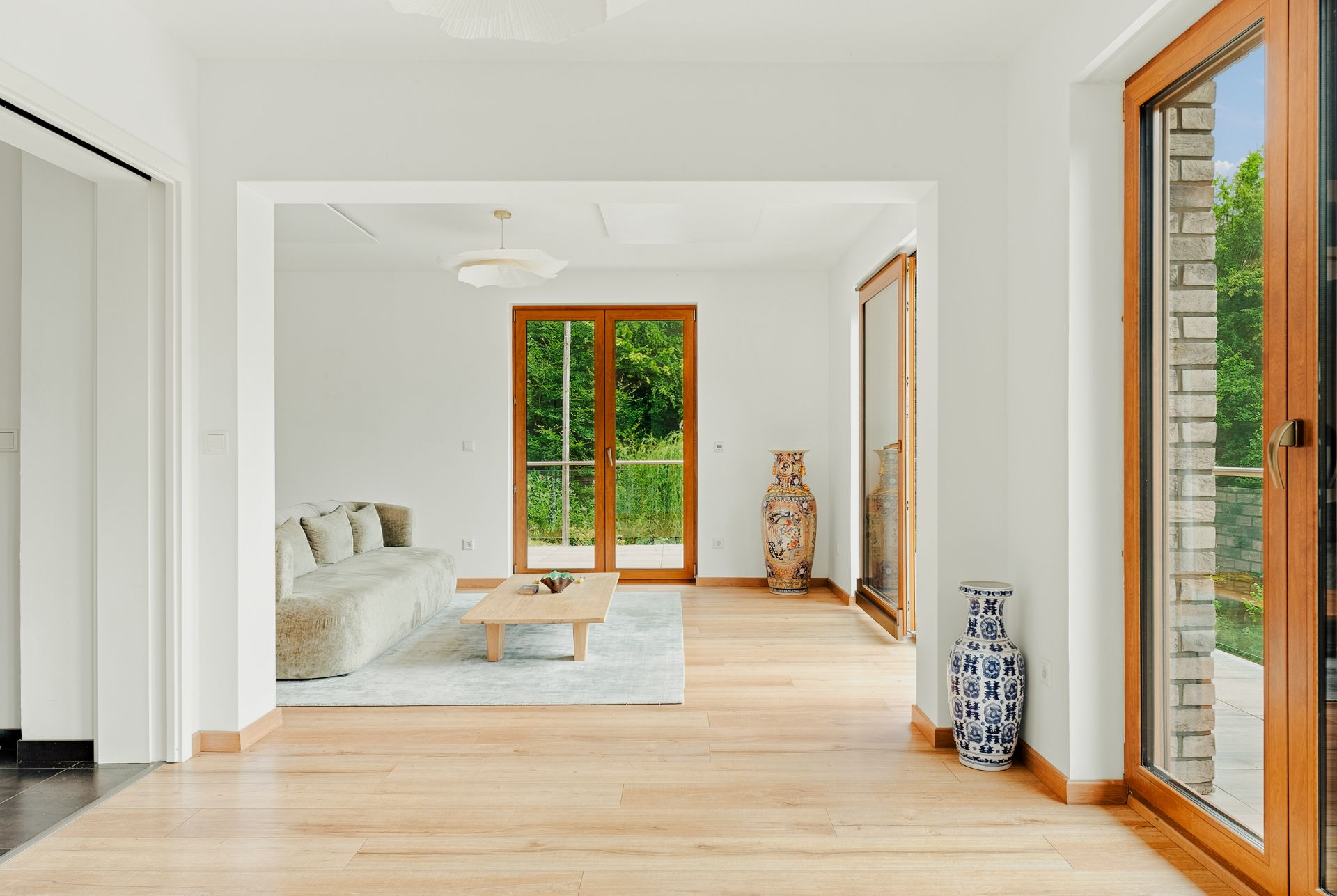 Helles Wohnzimmer mit Holzfußboden, Sofa, Couchtisch, großen Fenstern und zwei dekorativen Vasen.