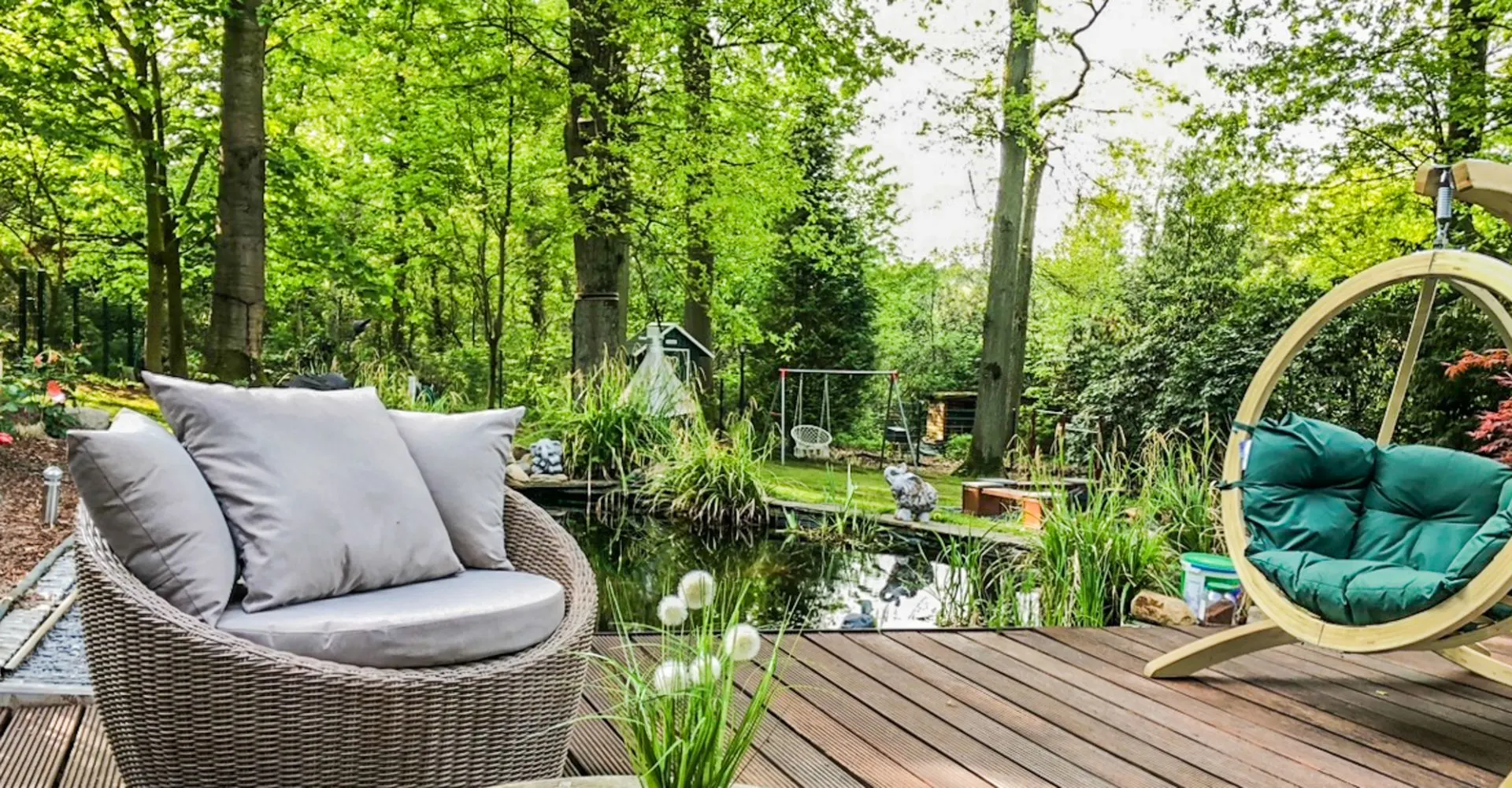 Holzterrasse mit modernen Sitzmöbeln, Teich und grünem Garten im Hintergrund.