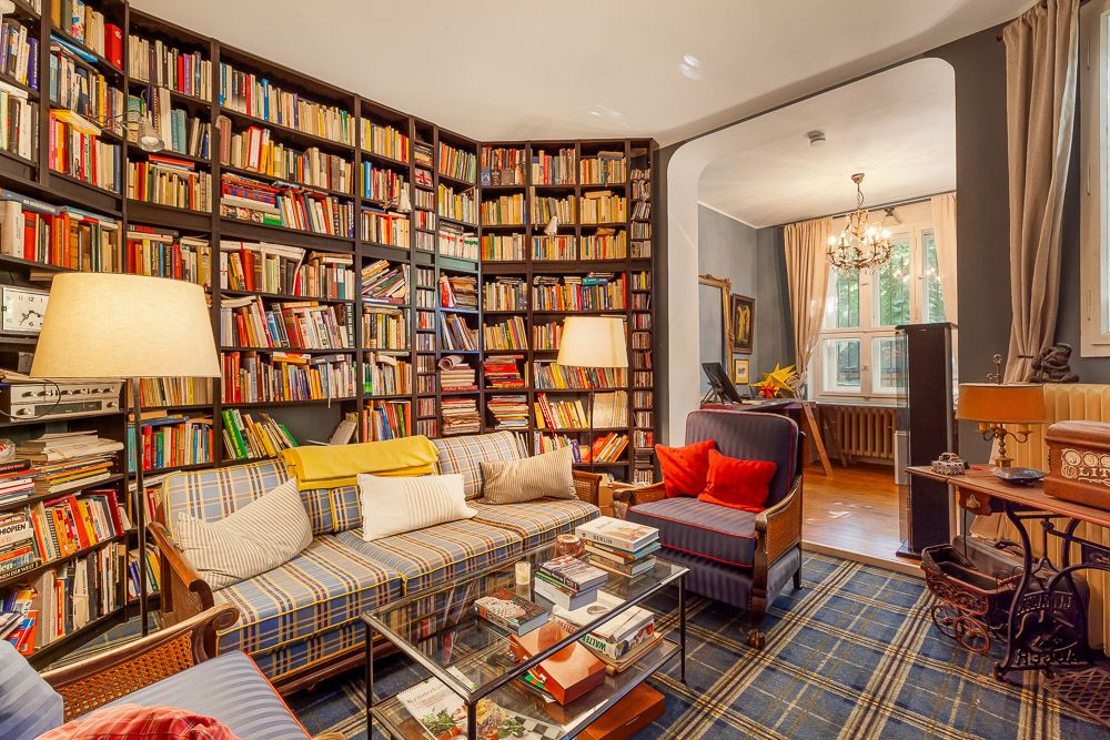 Gemütliches Wohnzimmer mit vielen Bücherregalen, Sofa, Sesseln und Stehlampen.