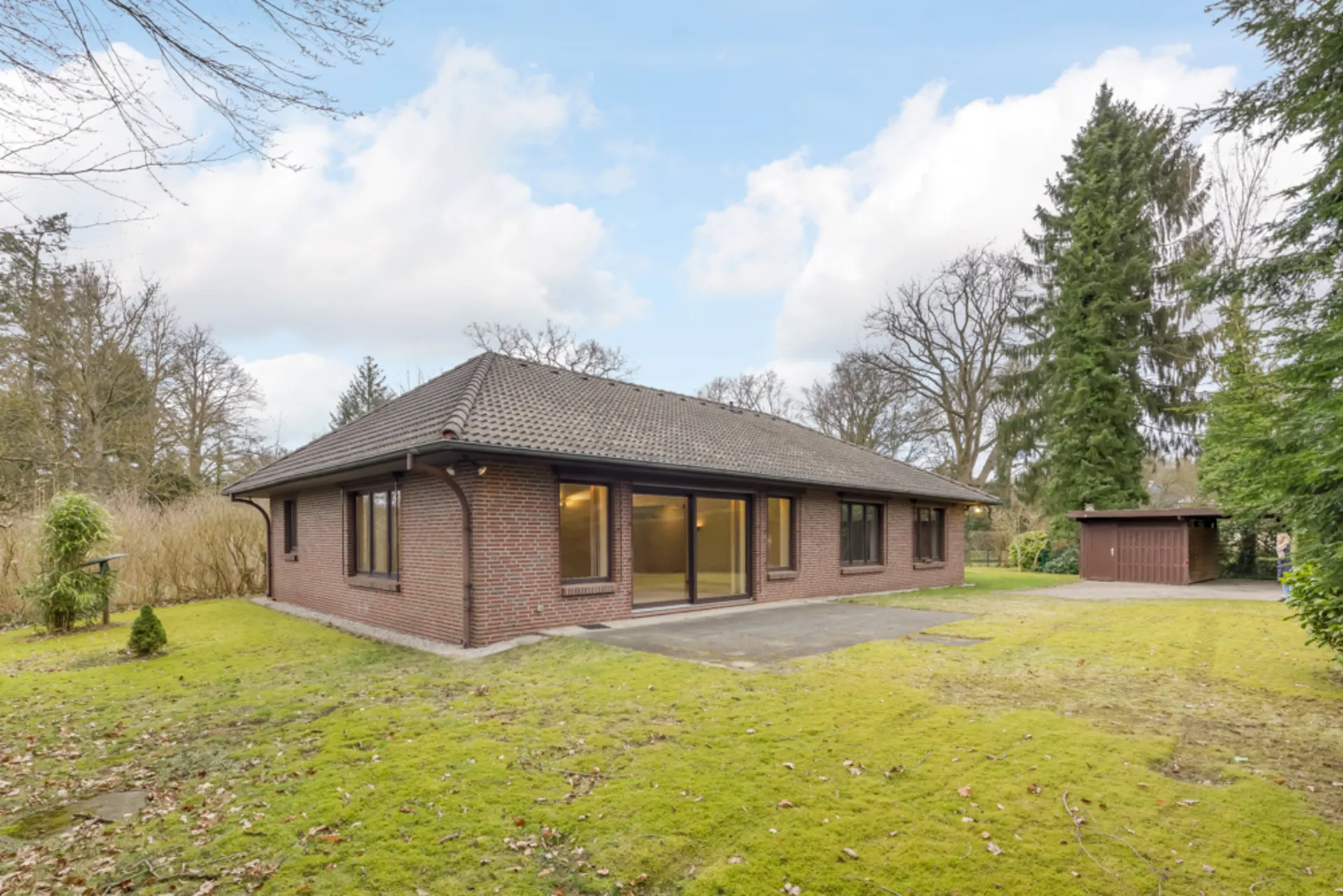 Backsteinbungalow mit großen Fenstern und Garten, daneben ein separates kleines Gebäude.