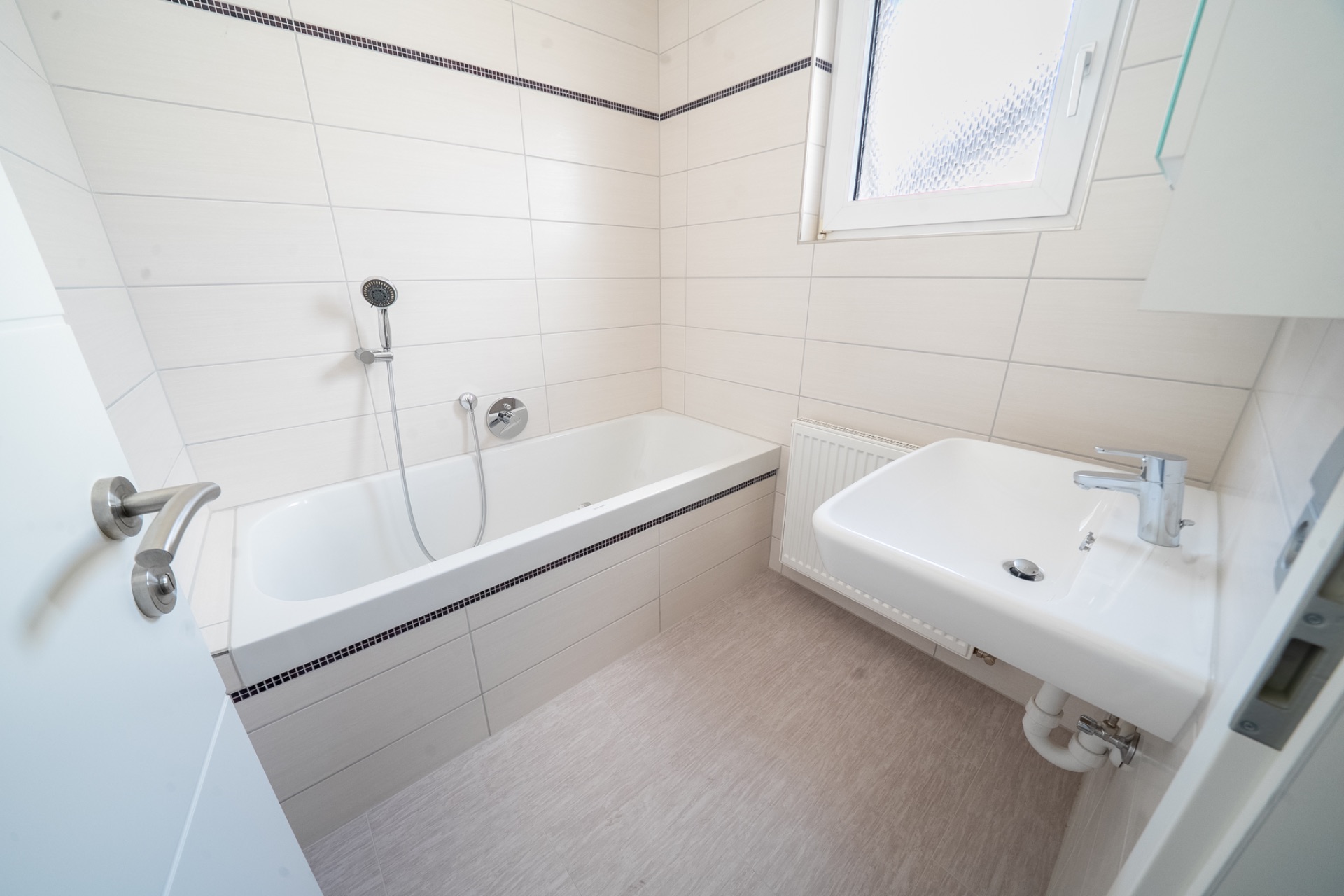 Helles Badezimmer mit Badewanne, Waschbecken und Fenster.