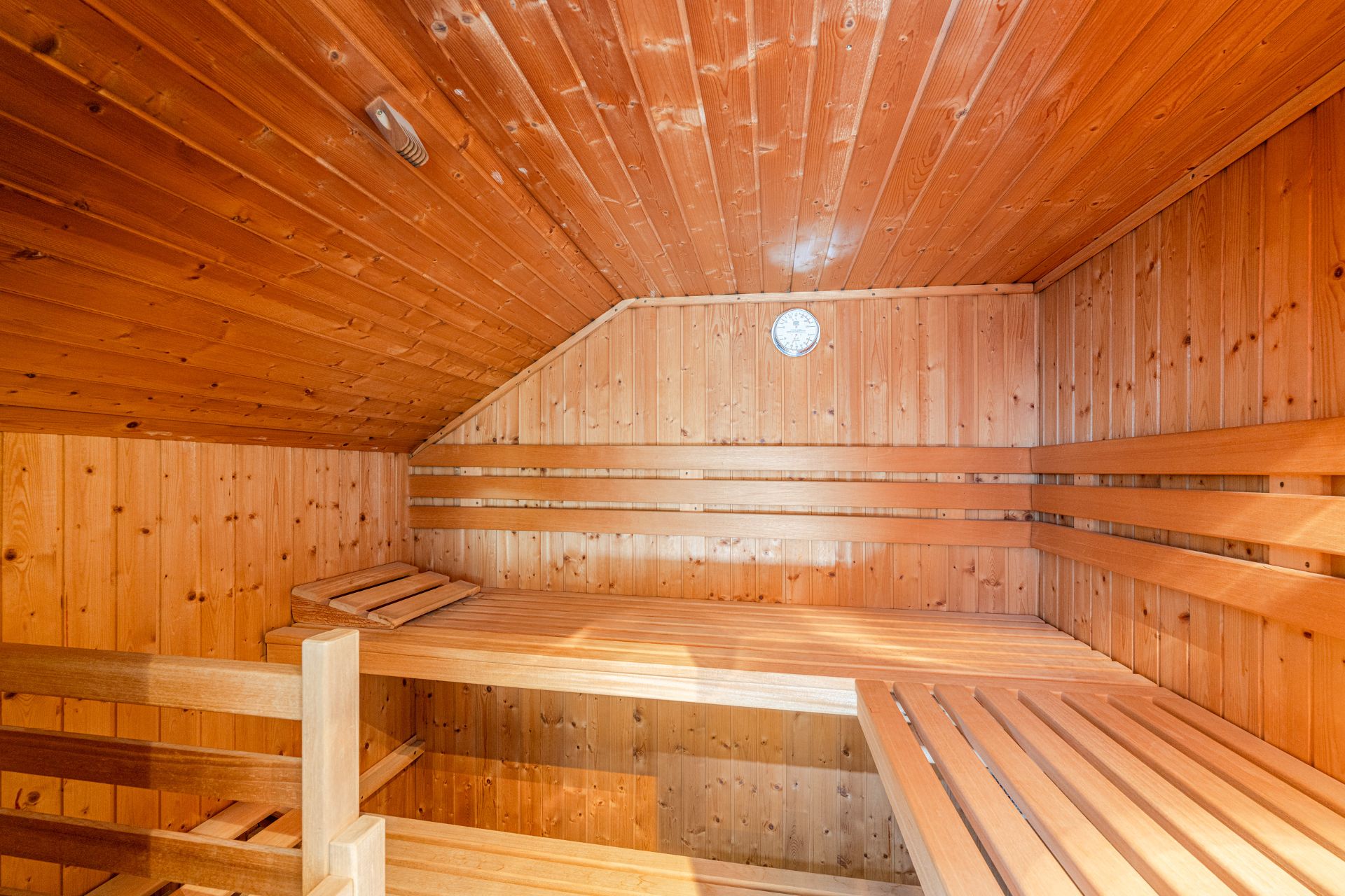 Innenraum einer holzverkleideten Sauna mit Sitzbänken und Thermometer an der Wand.