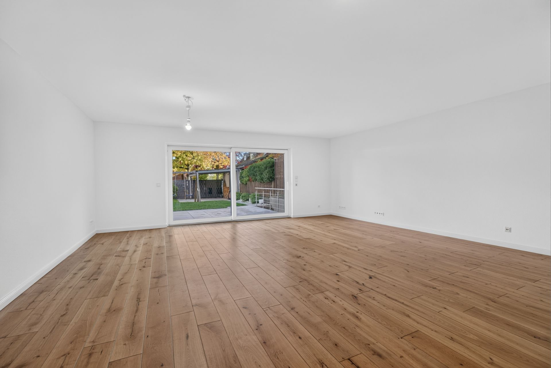 Leerer Raum mit Holzfußboden und großer Glas-Schiebetür zum Garten.