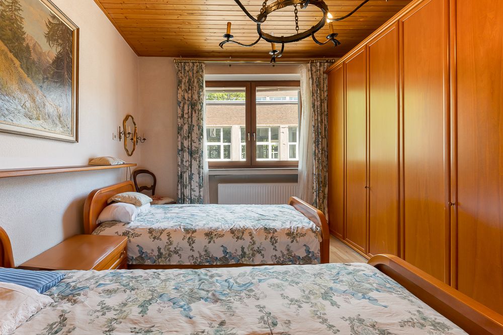Schlafzimmer mit zwei Einzelbetten, großen Holzschränken und einem Fenster mit Vorhängen.