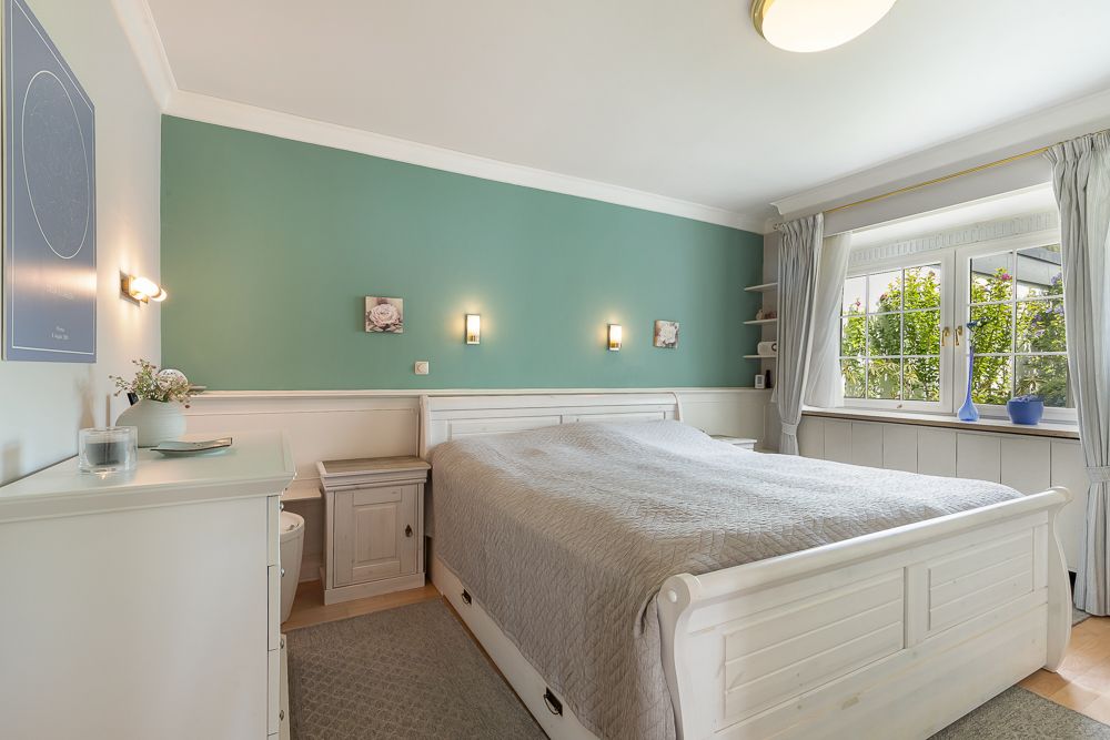 Helles Schlafzimmer mit Doppelbett, grüner Wand, Fenstern und weißen Möbeln.