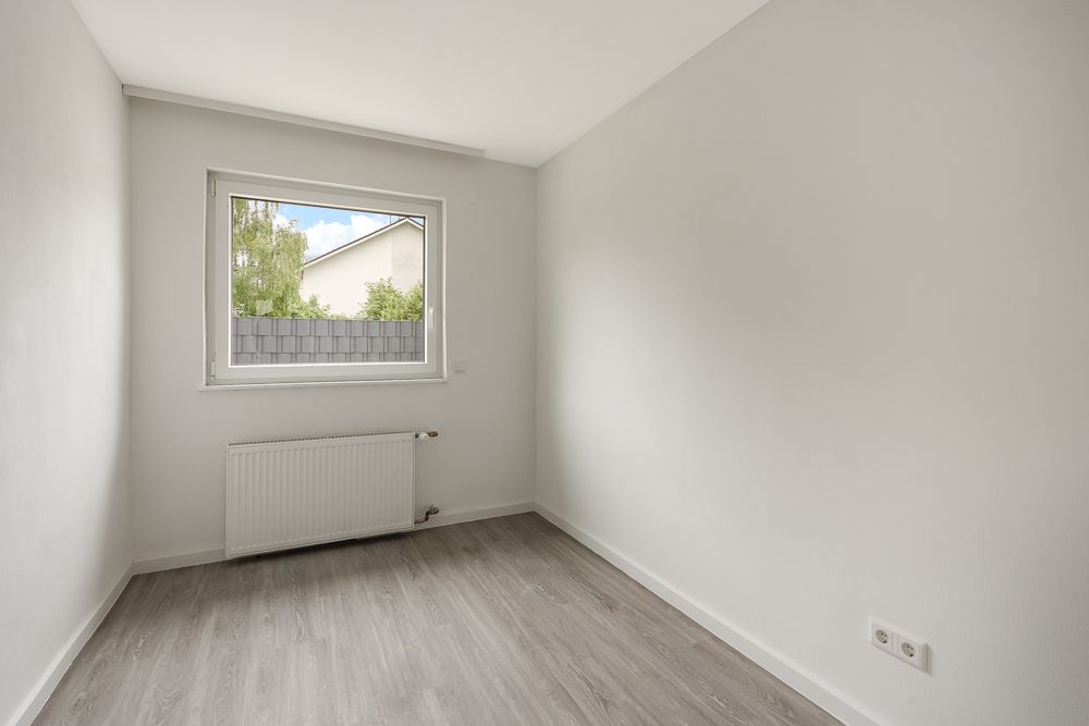 Leerer, schmaler Raum mit Fenster, Heizung und hellgrauem Boden.