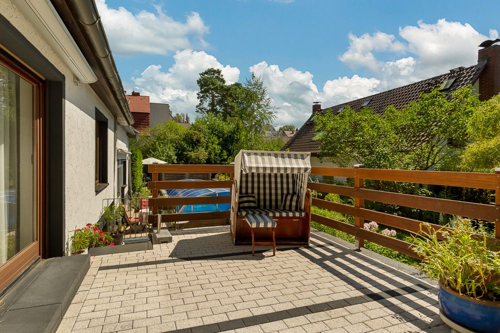 Sonnige Terrasse mit Strandkorb, Pflanzen und Blick auf Garten und Nachbarhäuser.