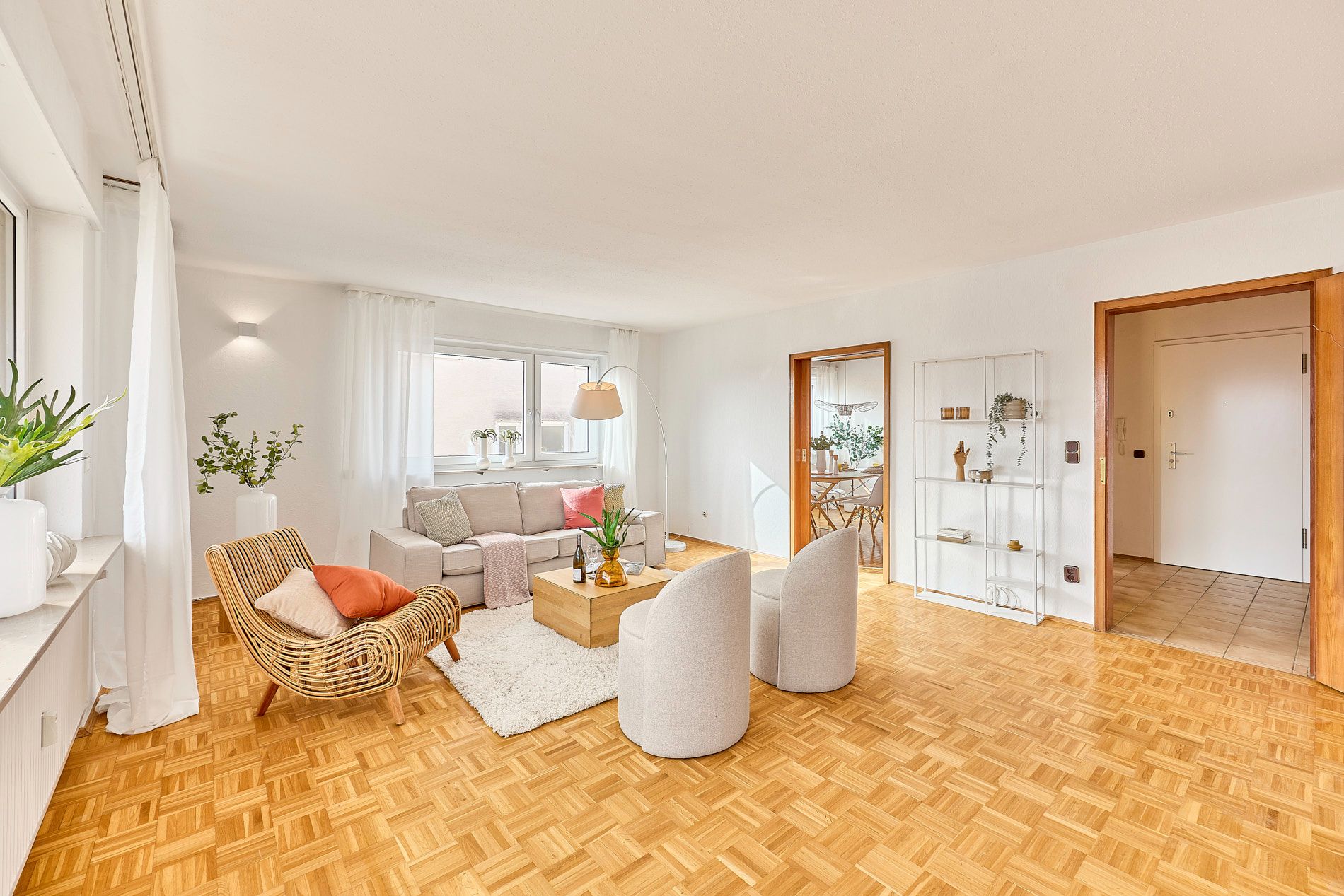 Helles Wohnzimmer mit Sofa, Sesseln, Rattanstuhl, Couchtisch und Parkettboden.