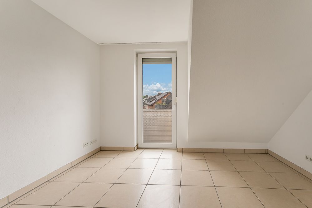 Heller leerer Raum mit Fliesenboden und Tür zu einem kleinen Balkon.