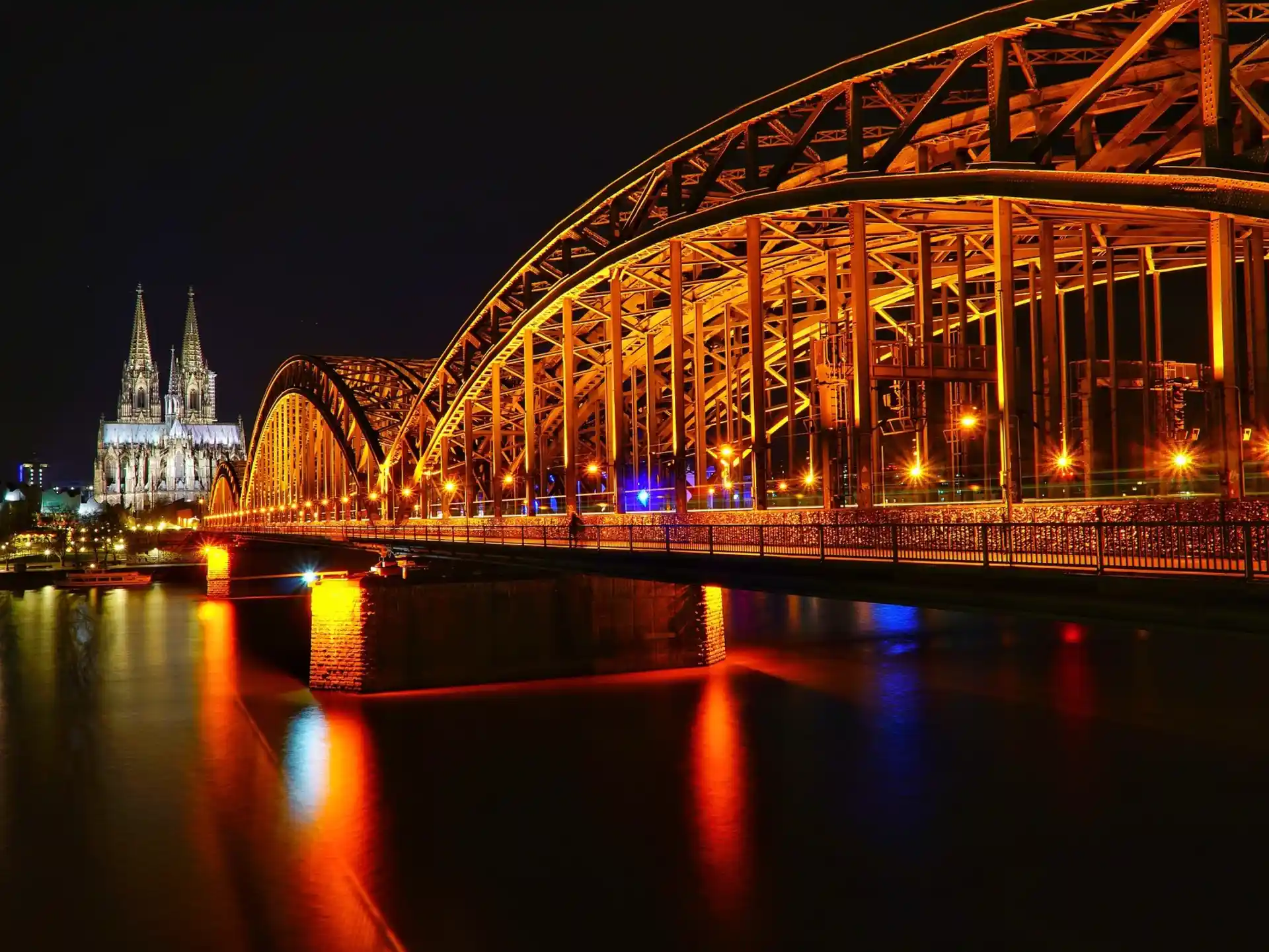 Große beleuchtete Brücke über einen Fluss bei Nacht, links eine Kirche mit zwei Türmen.