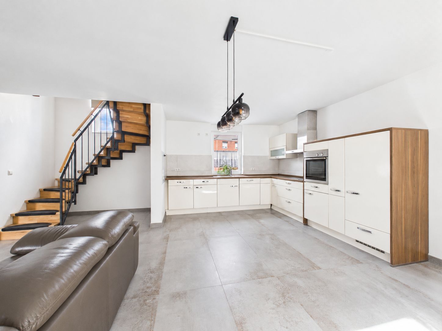 Moderne offene Küche mit weißen Schränken, braunem Sofa und Holztreppe.