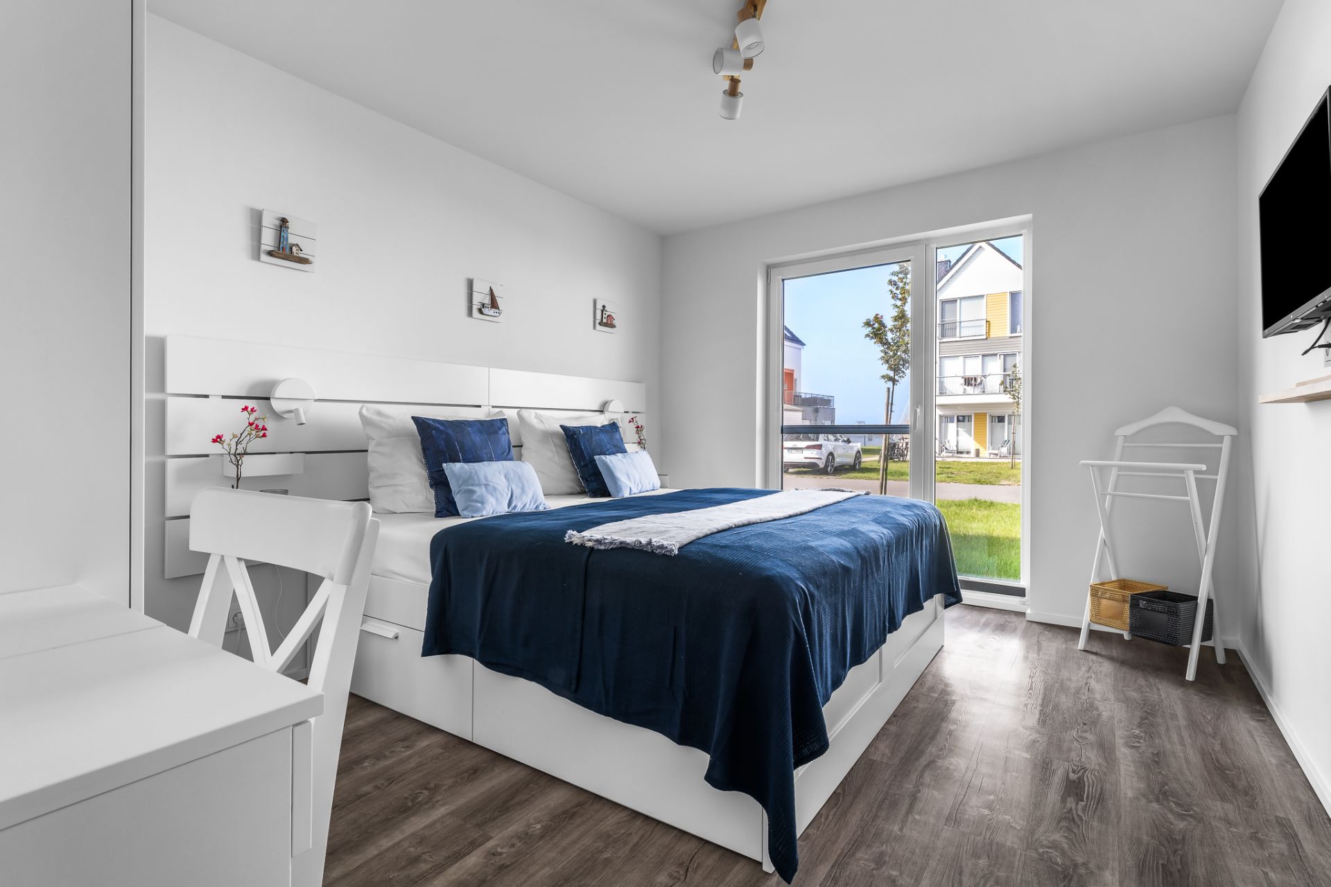Helles Schlafzimmer mit Doppelbett, Schreibtisch, großem Fenster und Blick nach draußen.