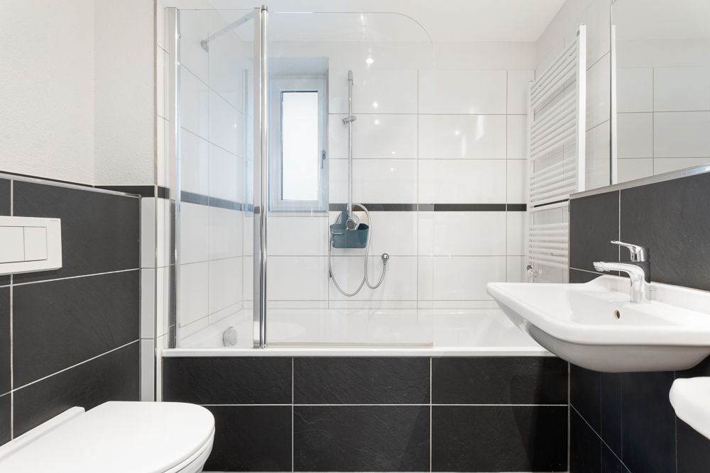 Modernes Badezimmer mit Badewanne, Dusche, Waschbecken, Toilette und Handtuchheizkörper.
