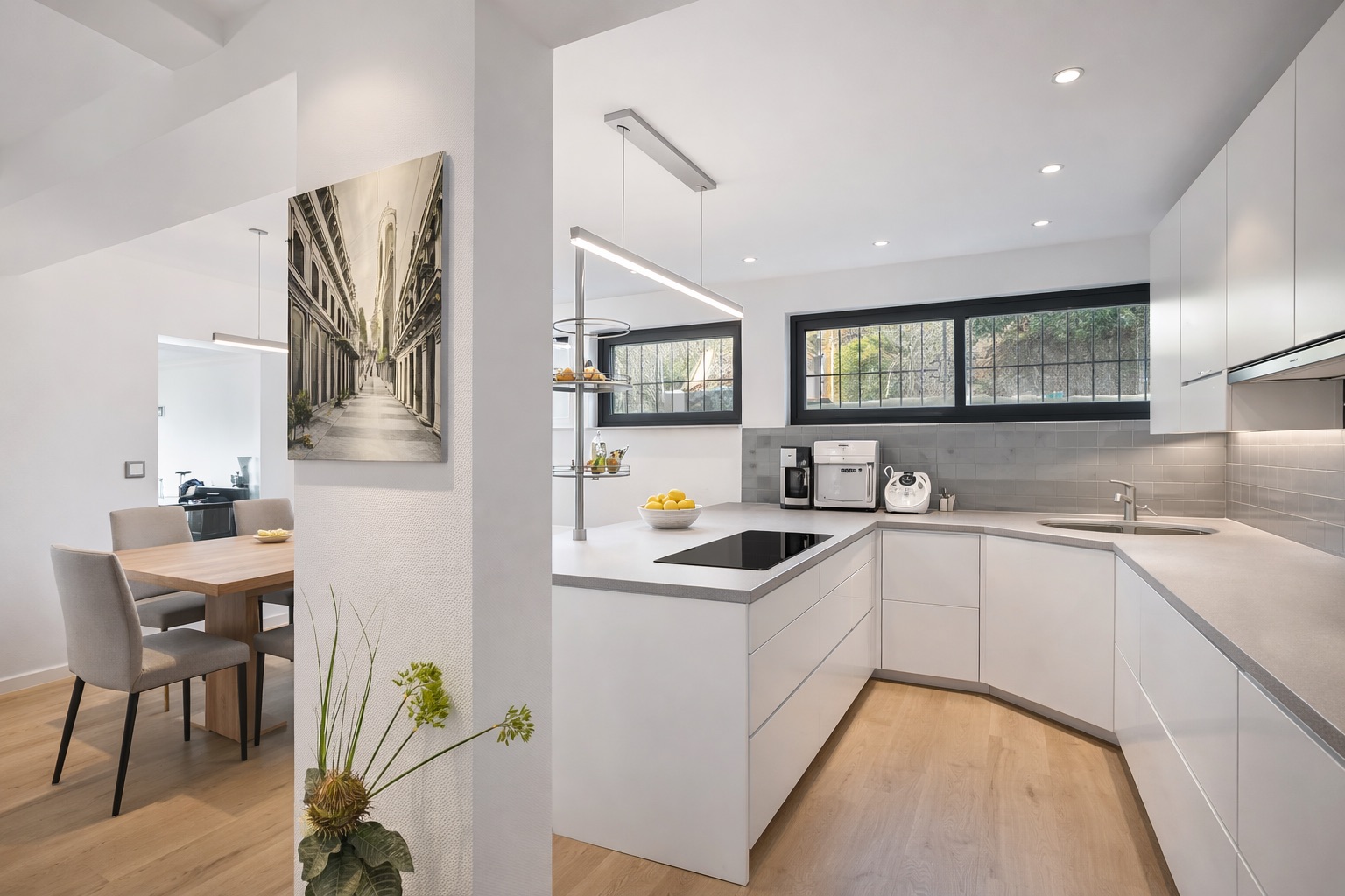 Moderne weiße Einbauküche mit Holzfußboden, großem Fenster und angrenzendem Essbereich.