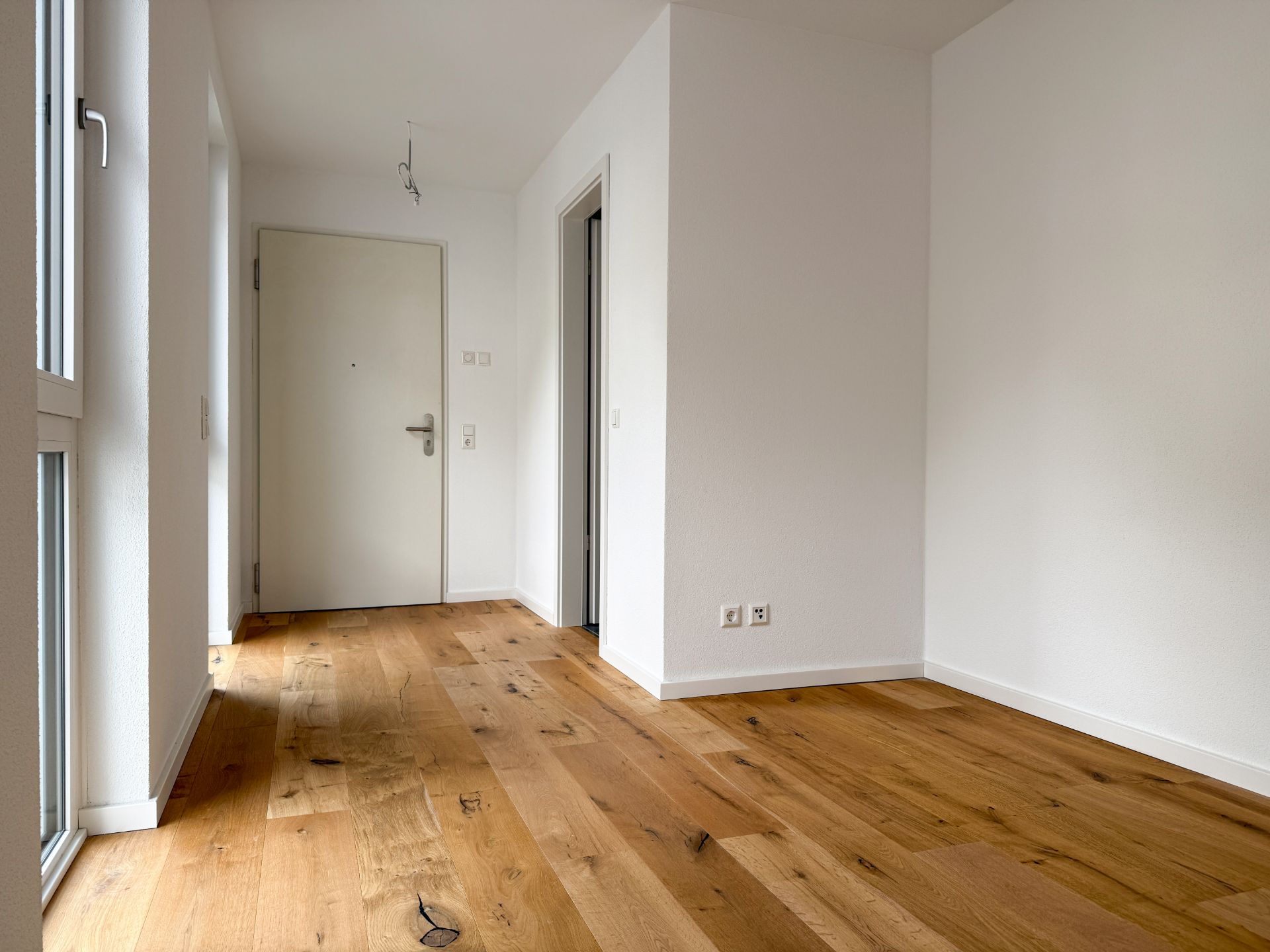 Heller Flur mit Holzboden, weißen Wänden und einer Eingangstür.