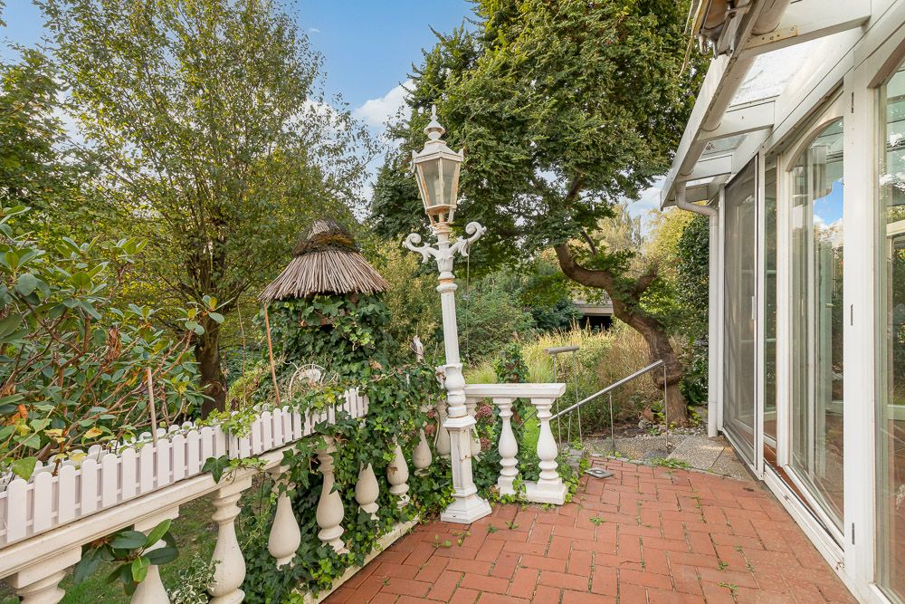 Terrasse mit weißem Geländer, alter Laterne und Blick in einen grünen Garten.