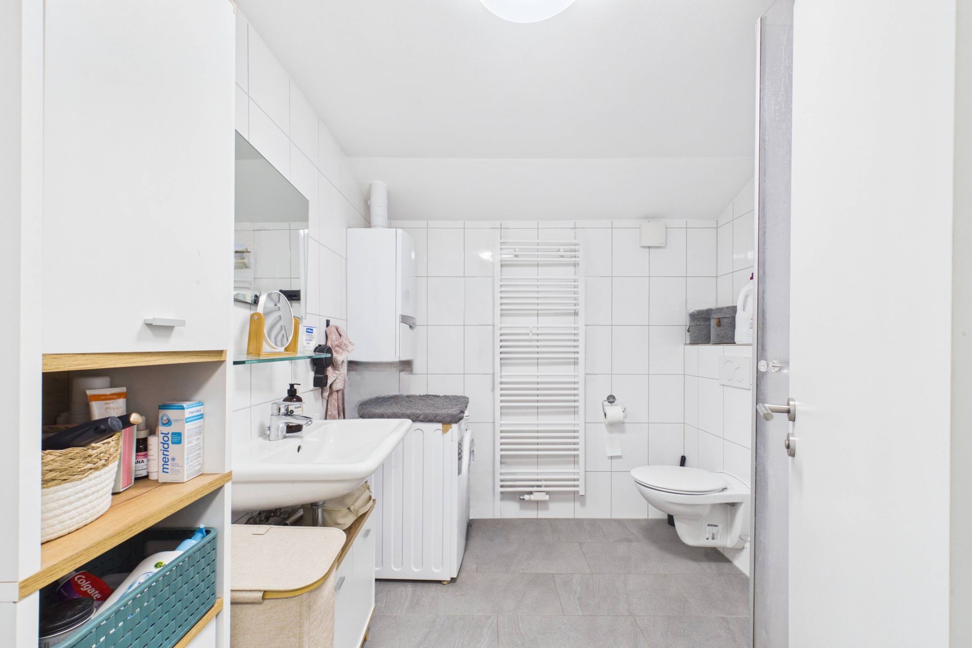 Modernes Badezimmer mit Waschbecken, Spiegelschrank, Waschmaschine und Wandtoilette.
