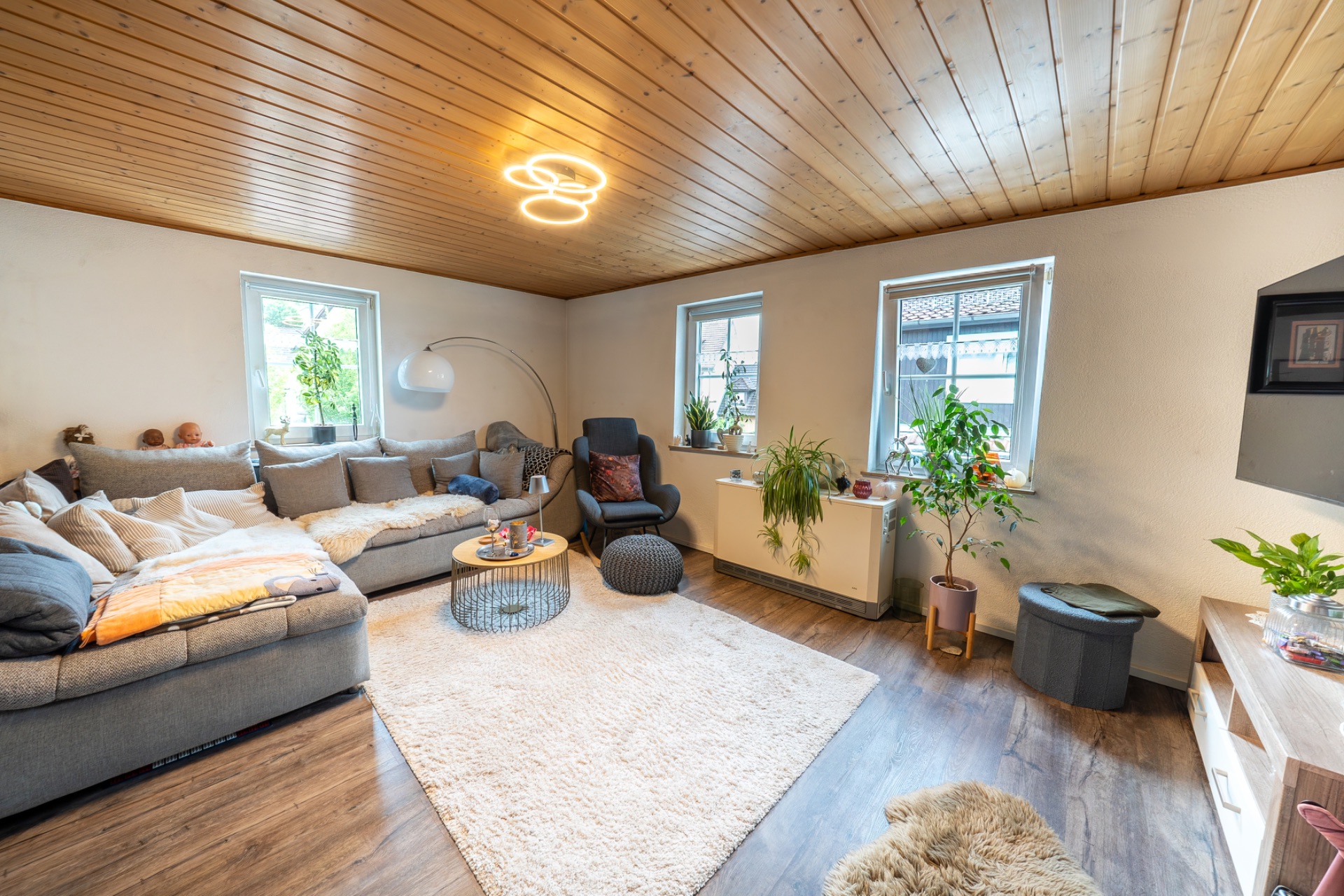 Helles Wohnzimmer mit Ecksofa, Teppich, Pflanzen und Holzdecke.