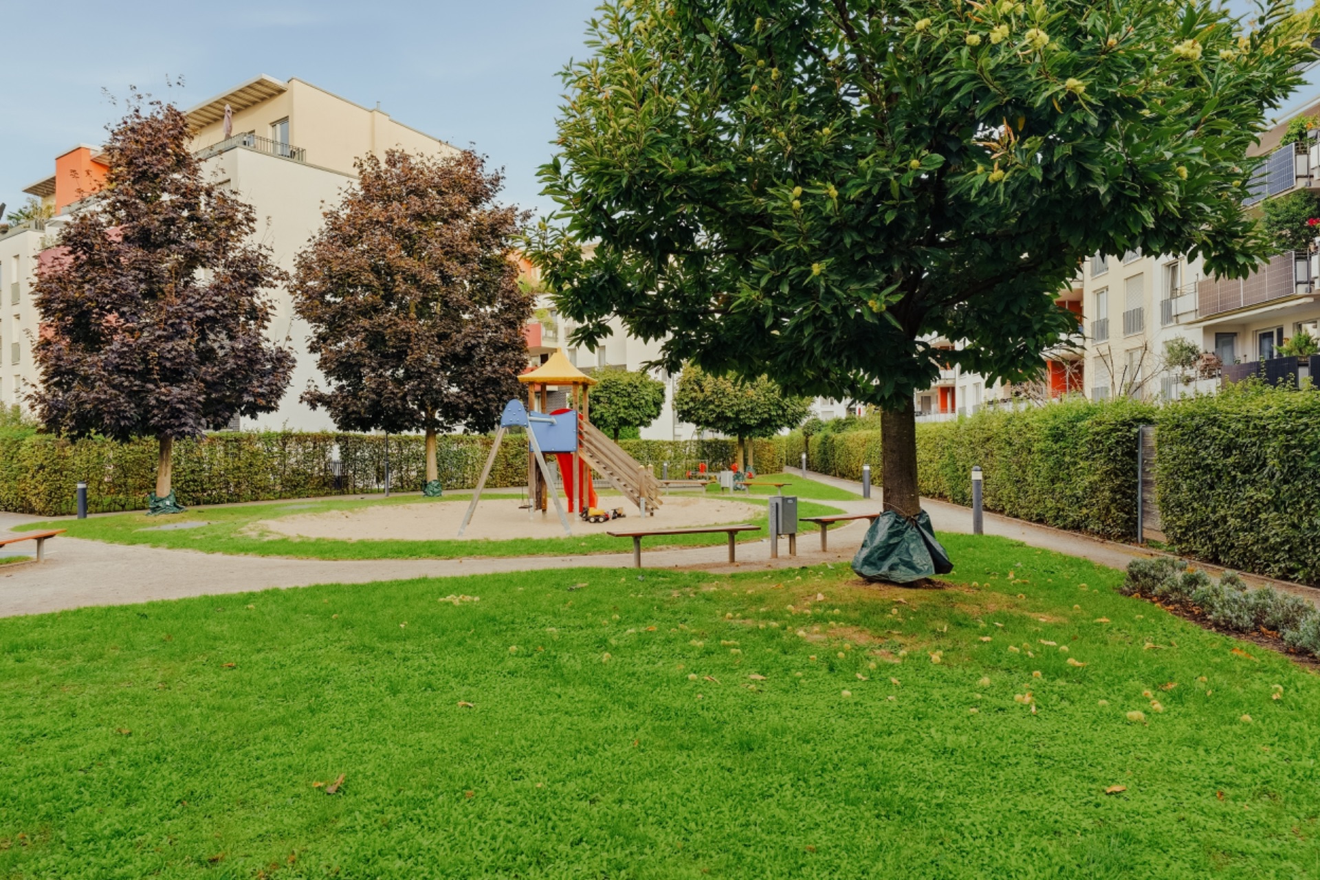 Grüne Wohnanlage mit Spielplatz, Rasenfläche, Bäumen und umgebenden Wohngebäuden.