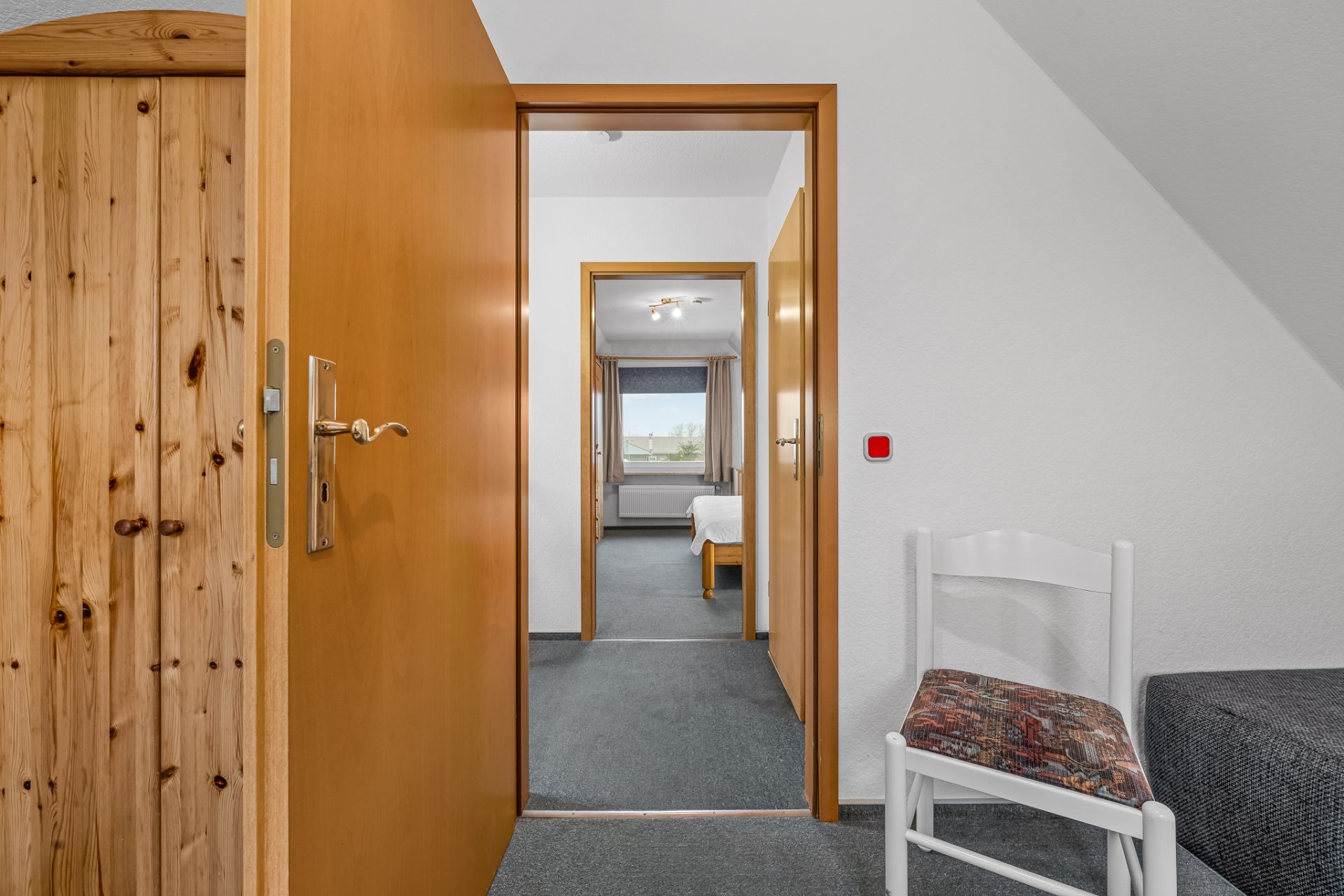 Offene Holztür mit Blick in einen Flur und ein Zimmer mit Fenster und Bett.