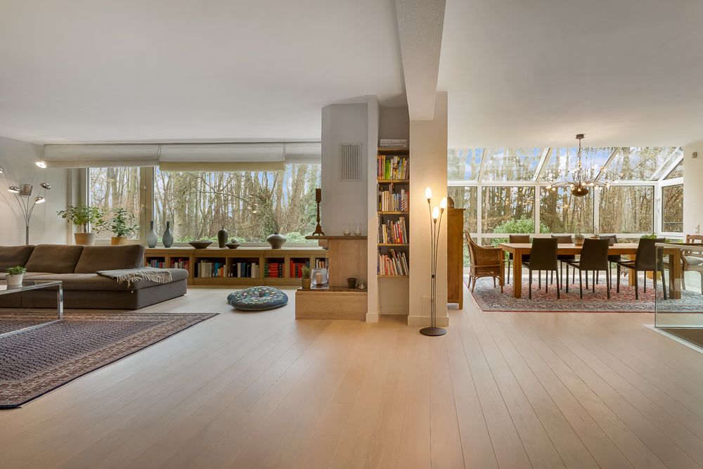 Helles Wohnzimmer mit Sofa und Regal, daneben Essbereich mit großem Tisch und Glasfront.