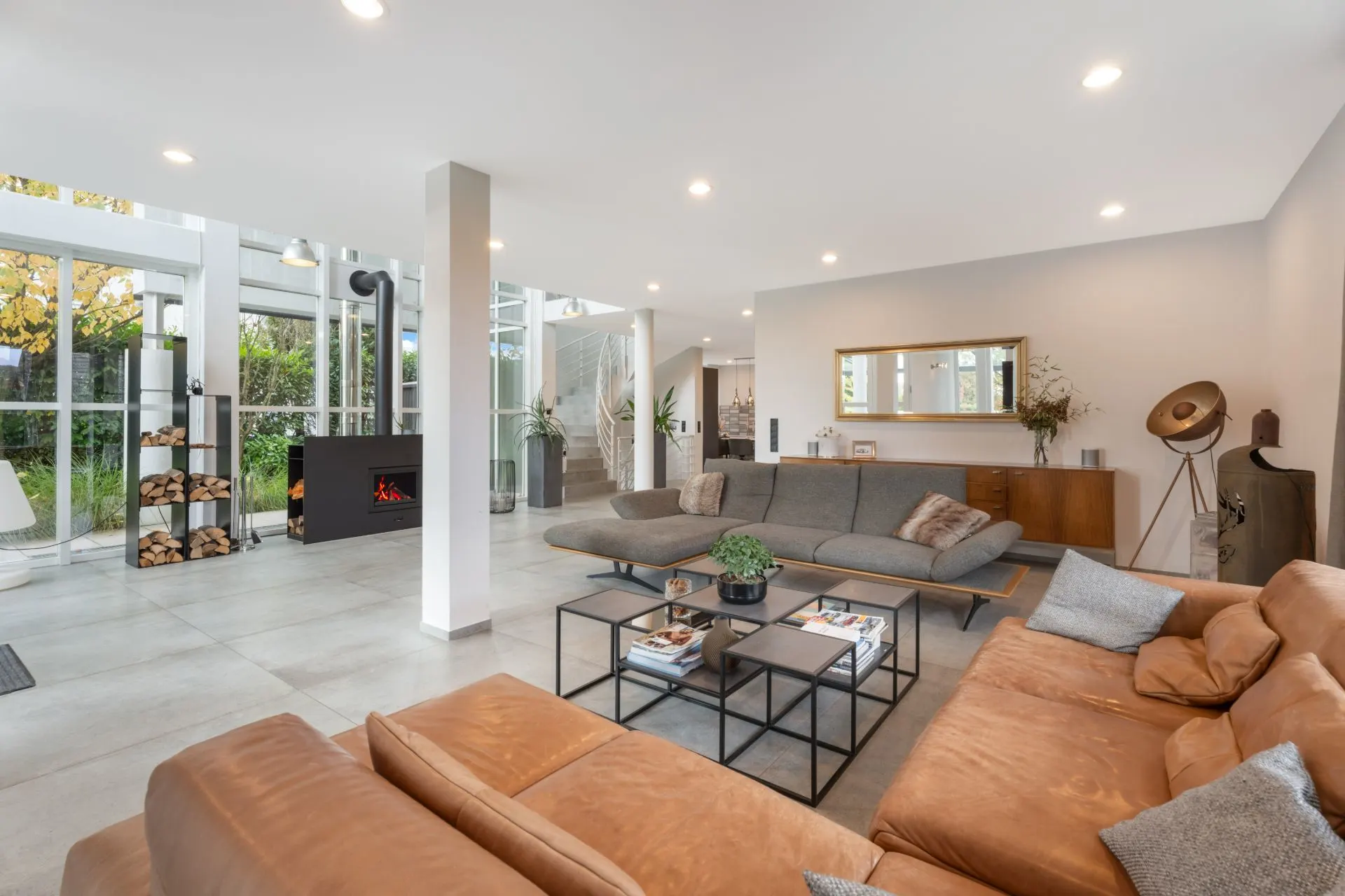 Modernes Wohnzimmer mit großen Sofas, Kamin und Glaswänden, Blick auf Garten.