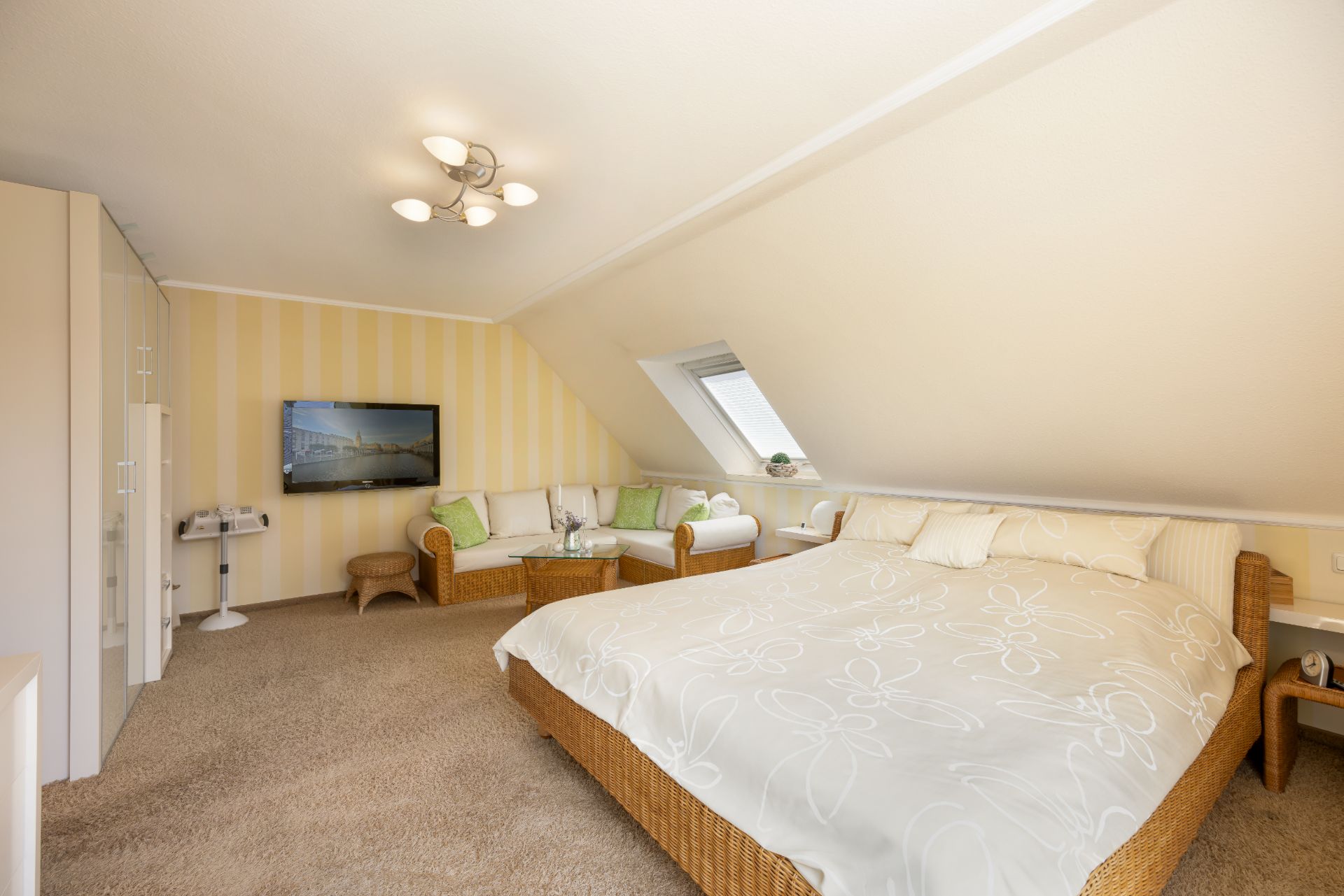 Helles Schlafzimmer mit Doppelbett, Sofa, Fernseher und Dachfenster unter einer Schräge.