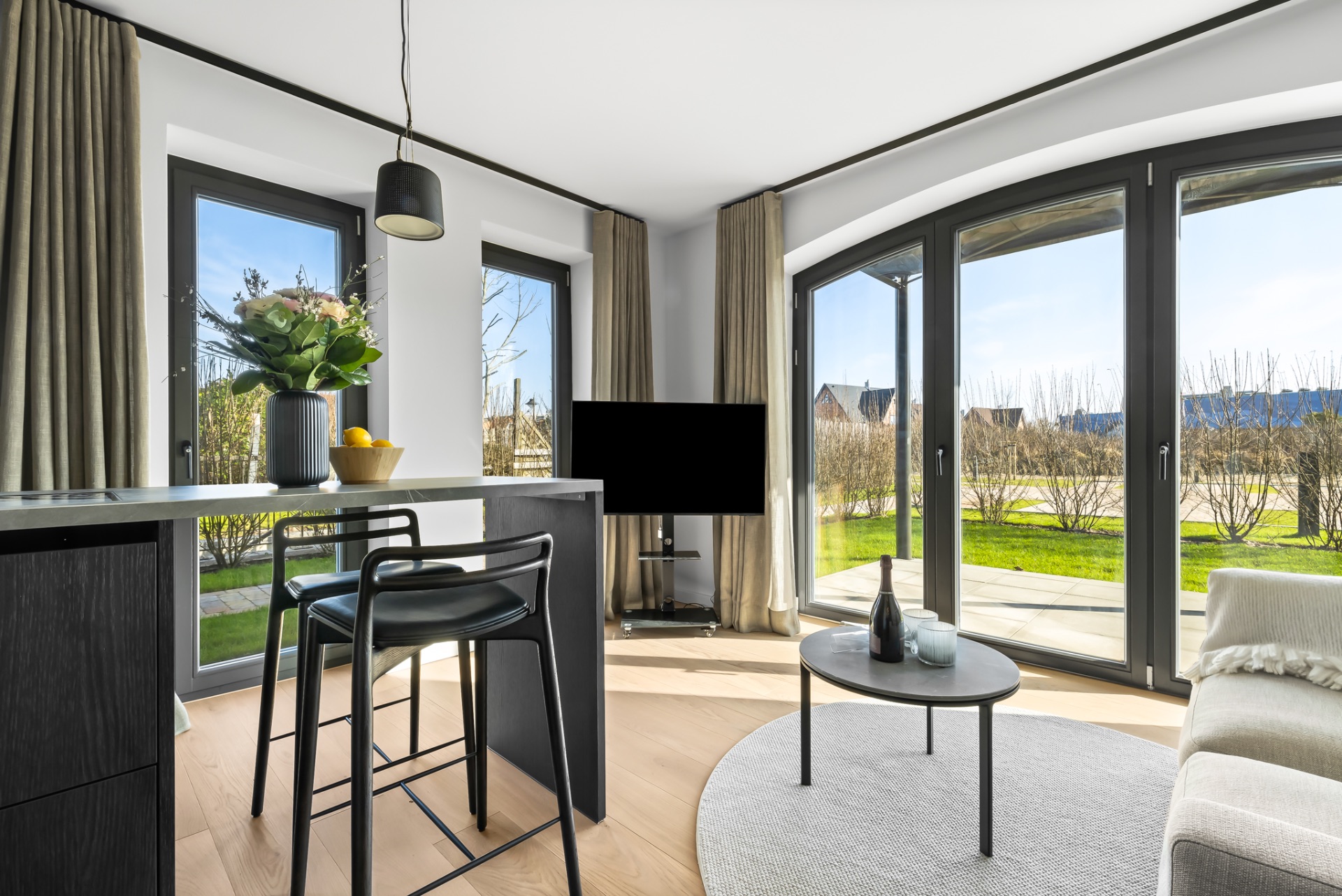 Helles Wohnzimmer mit großen Fenstern, Sofa, Couchtisch und Bartisch mit Stühlen.