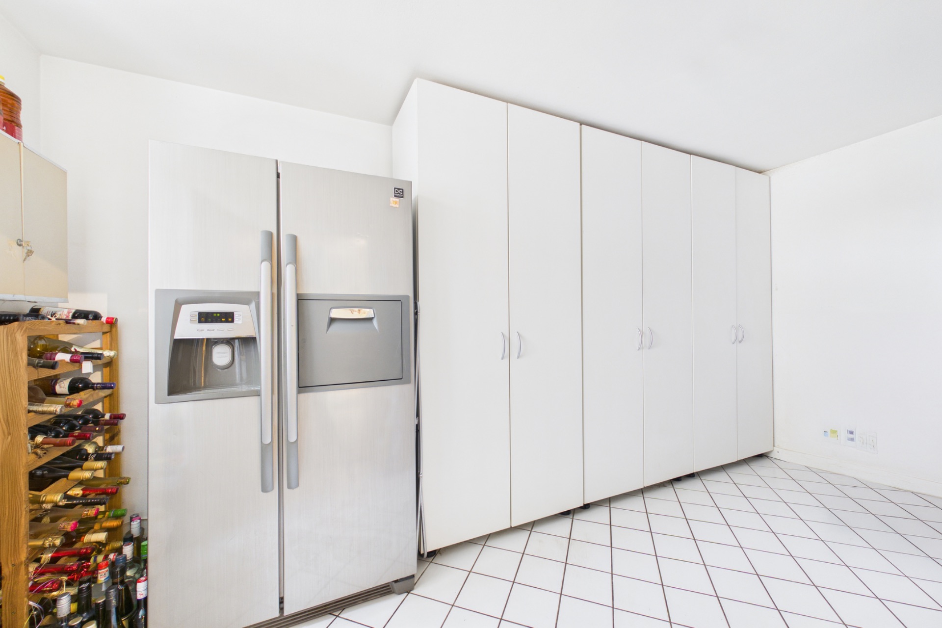 Küche mit großem Kühlschrank, weißen Einbauschränken und Weinregal auf Fliesenboden.