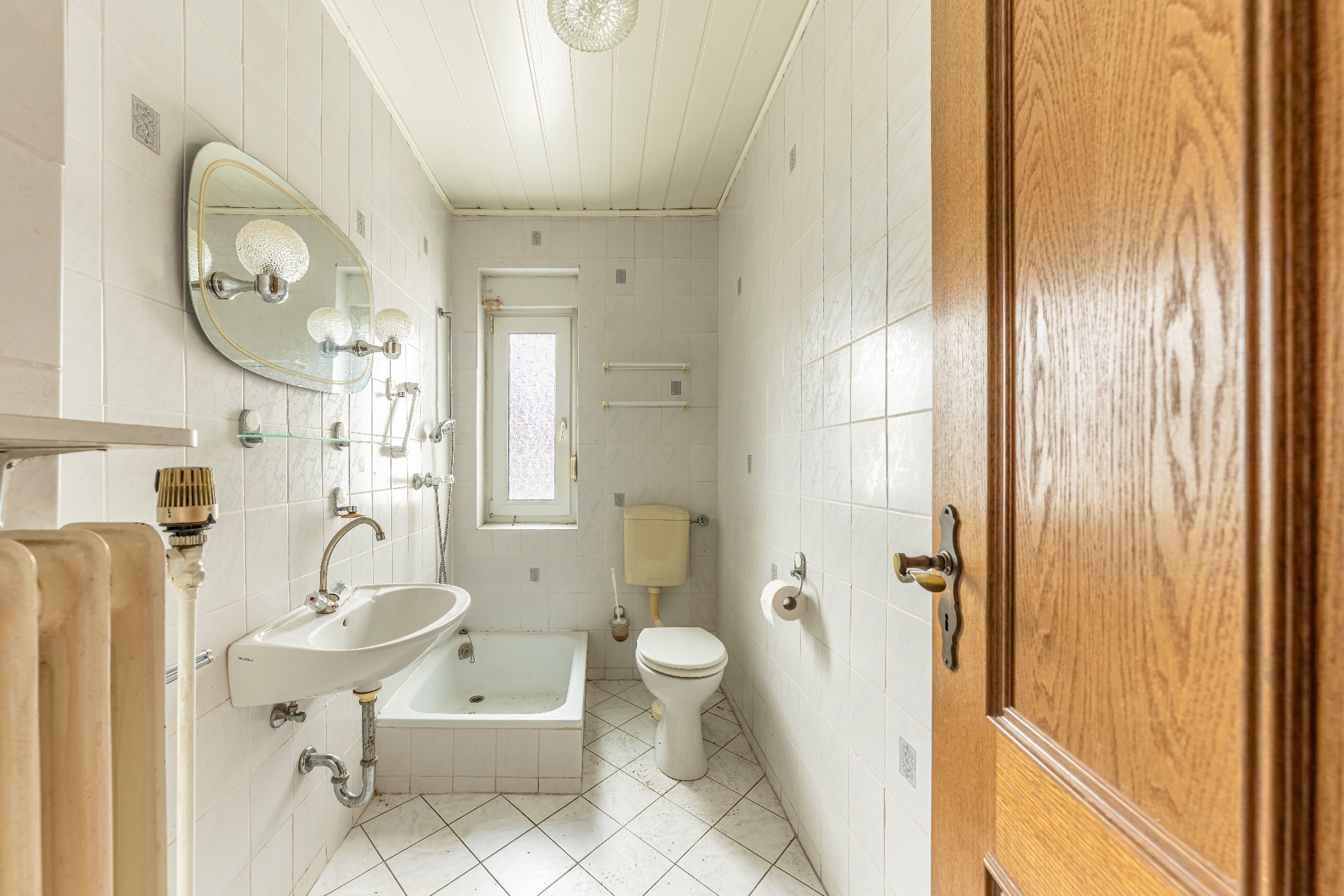 Helles Badezimmer mit Waschbecken, Toilette, Dusche und Fenster, alle Wände sind gefliest.