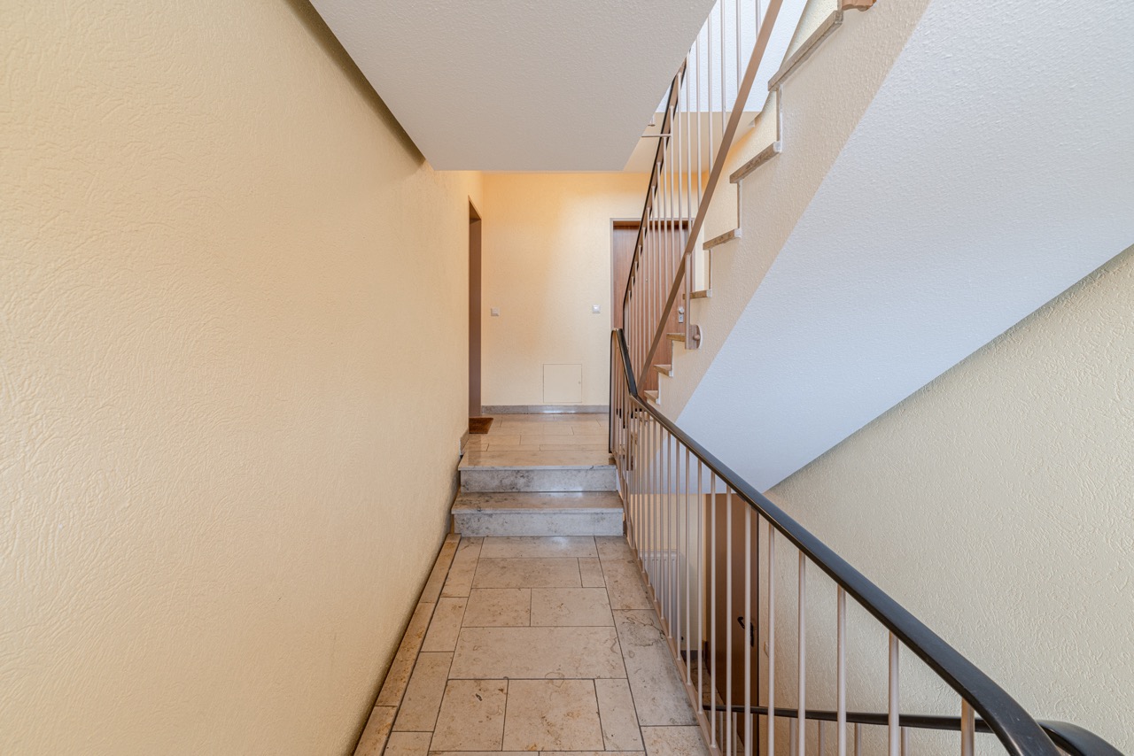 Heller Treppenhausflur mit Fliesenboden und Geländer, Türen im Hintergrund.