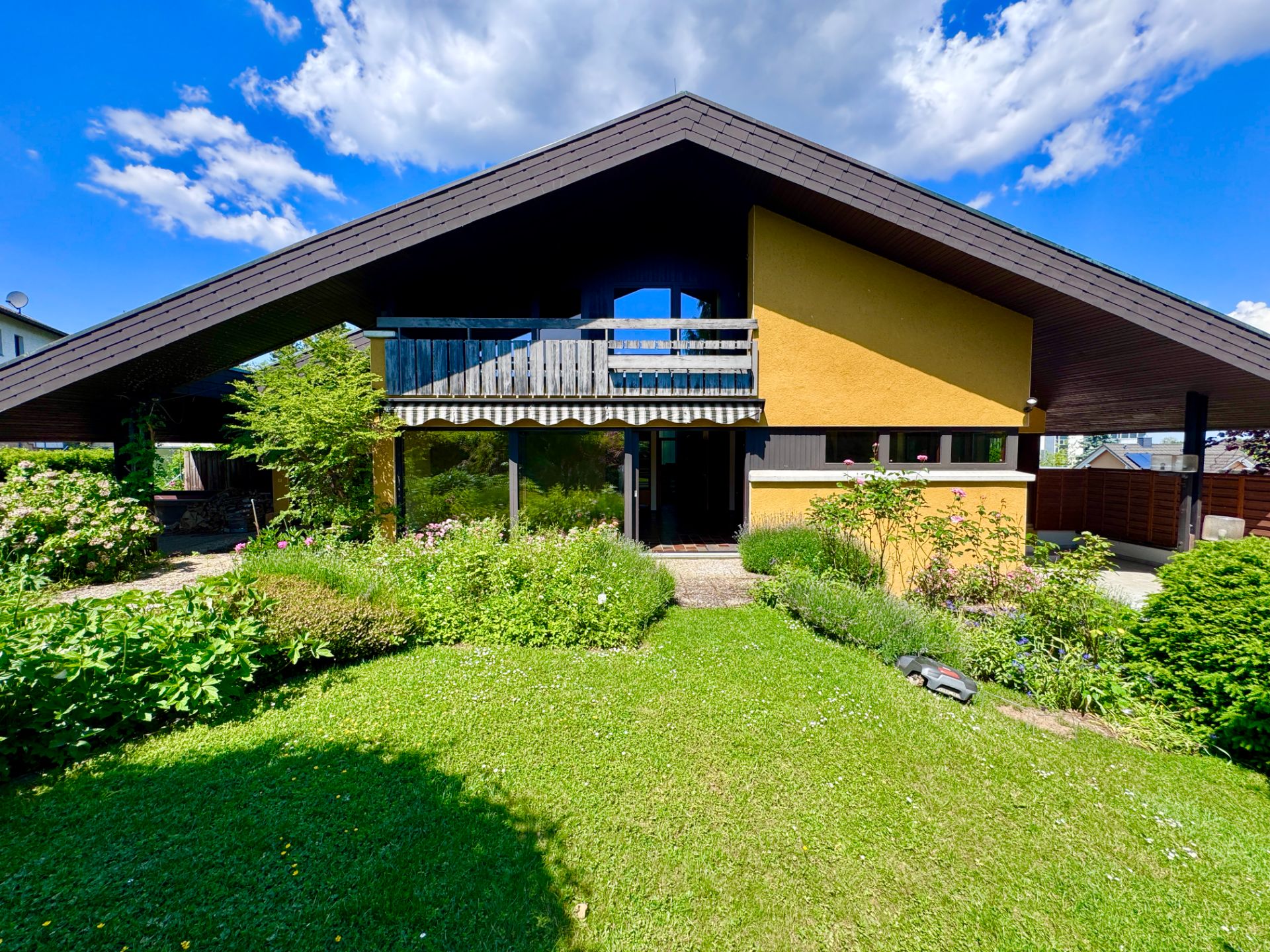 Modernes Haus mit großem Dach, Balkon und gepflegtem Garten im Vordergrund.