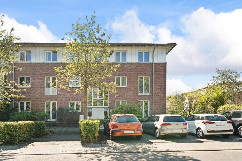 Dreistöckiges Wohnhaus aus rotem Backstein mit parkenden Autos und Bäumen davor.