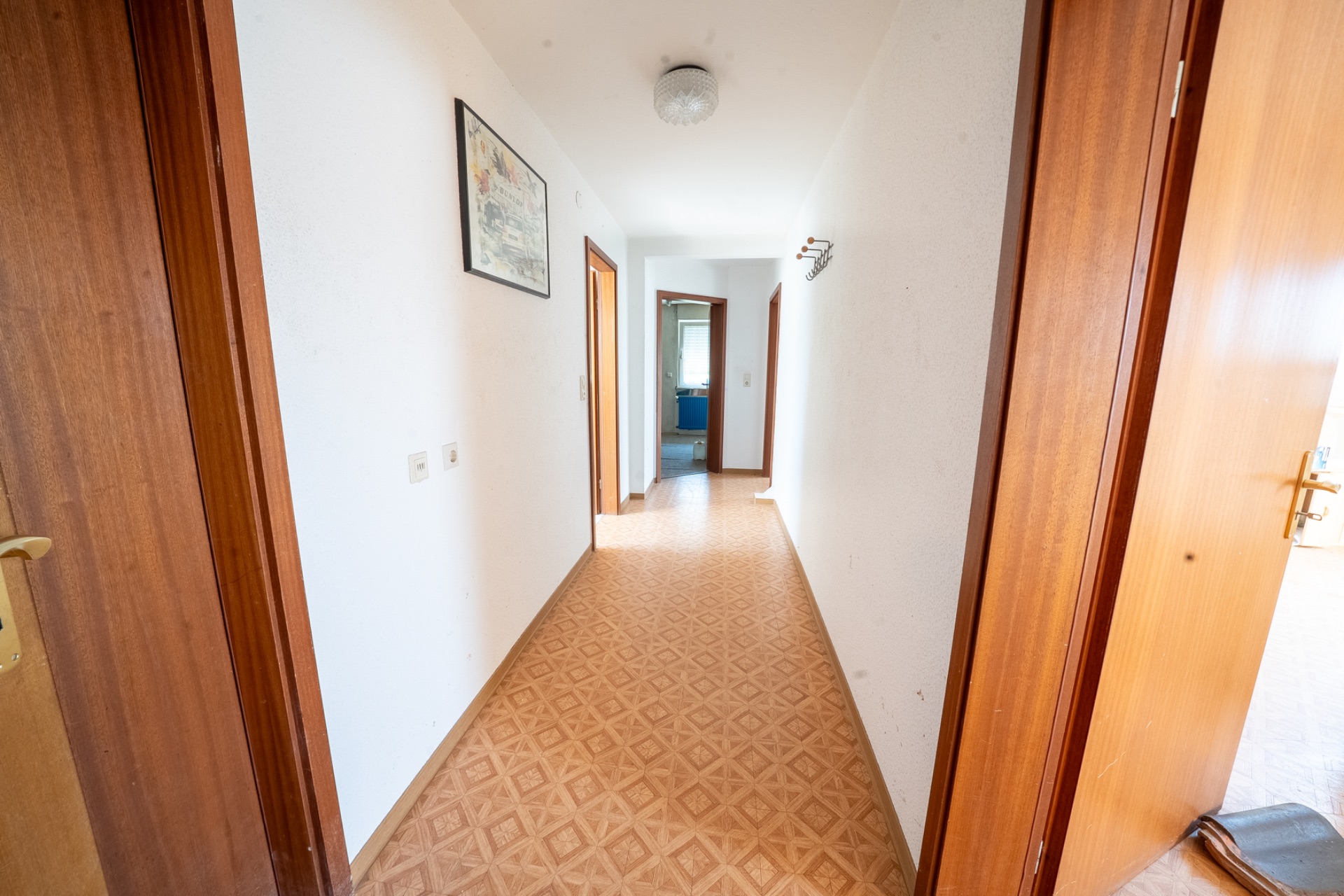 Heller Flur mit Holztüren, weißer Wand und Bild an der Wand.