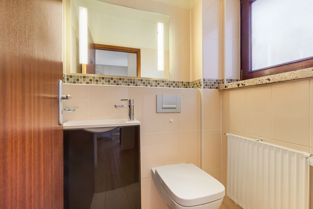 Modernes, kleines Badezimmer mit Wandtoilette, Waschbecken, Spiegel und Fenster.