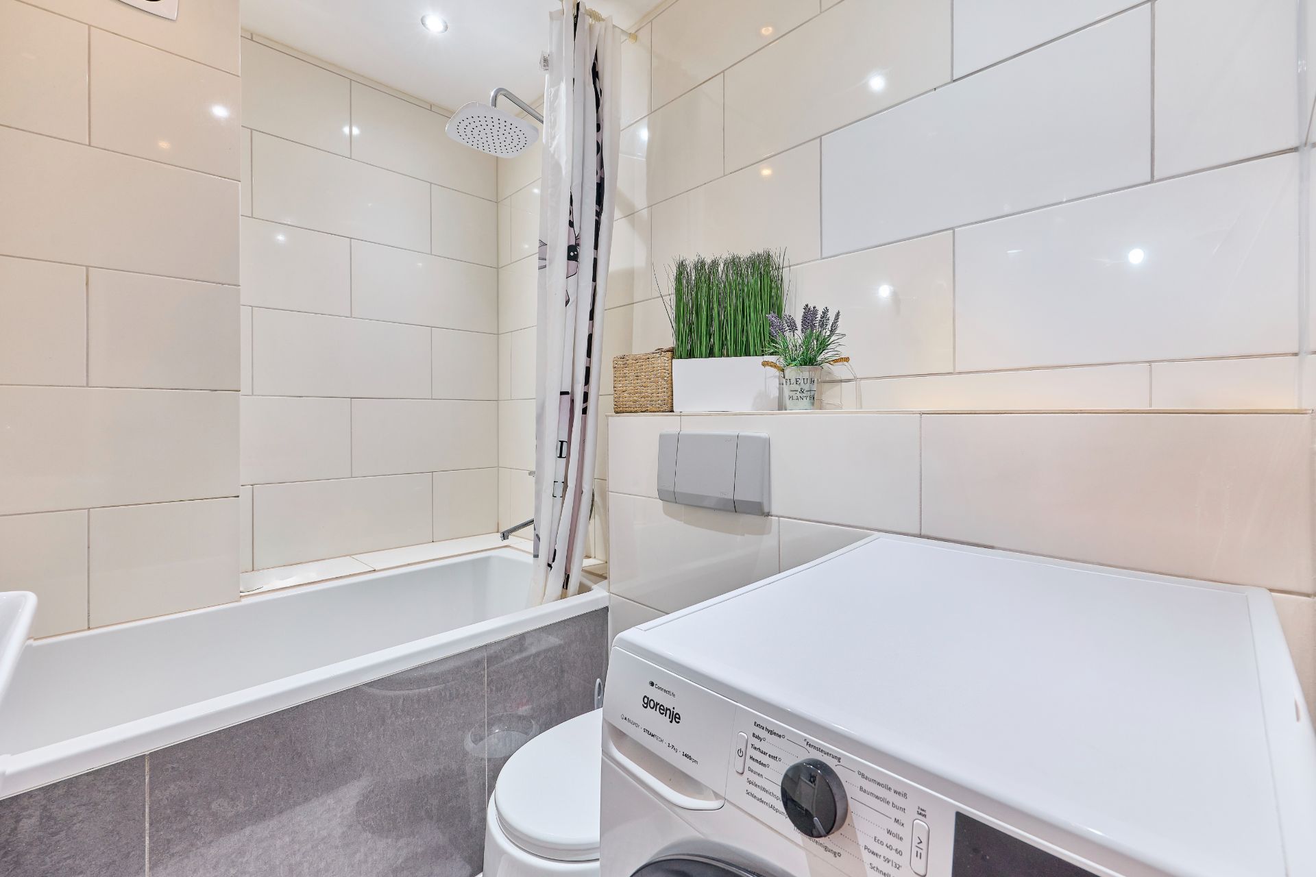Modernes Badezimmer mit Badewanne, Waschmaschine und Dekopflanzen auf einem Regal.