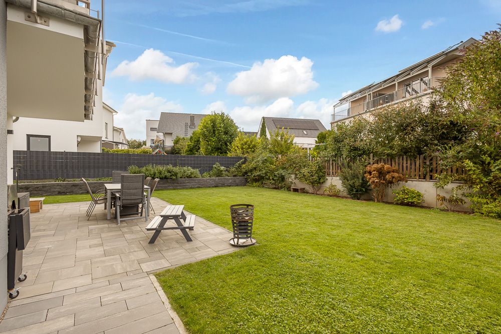 Garten mit Rasen, Terrasse, Sitzbank, Esstisch und Stühlen, umgeben von Hecken und Zäunen.