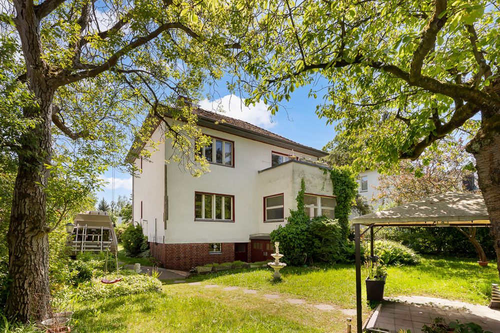 Zwei­stöckiges weißes Wohnhaus mit Garten, Bäumen und Pavillon im Vordergrund.