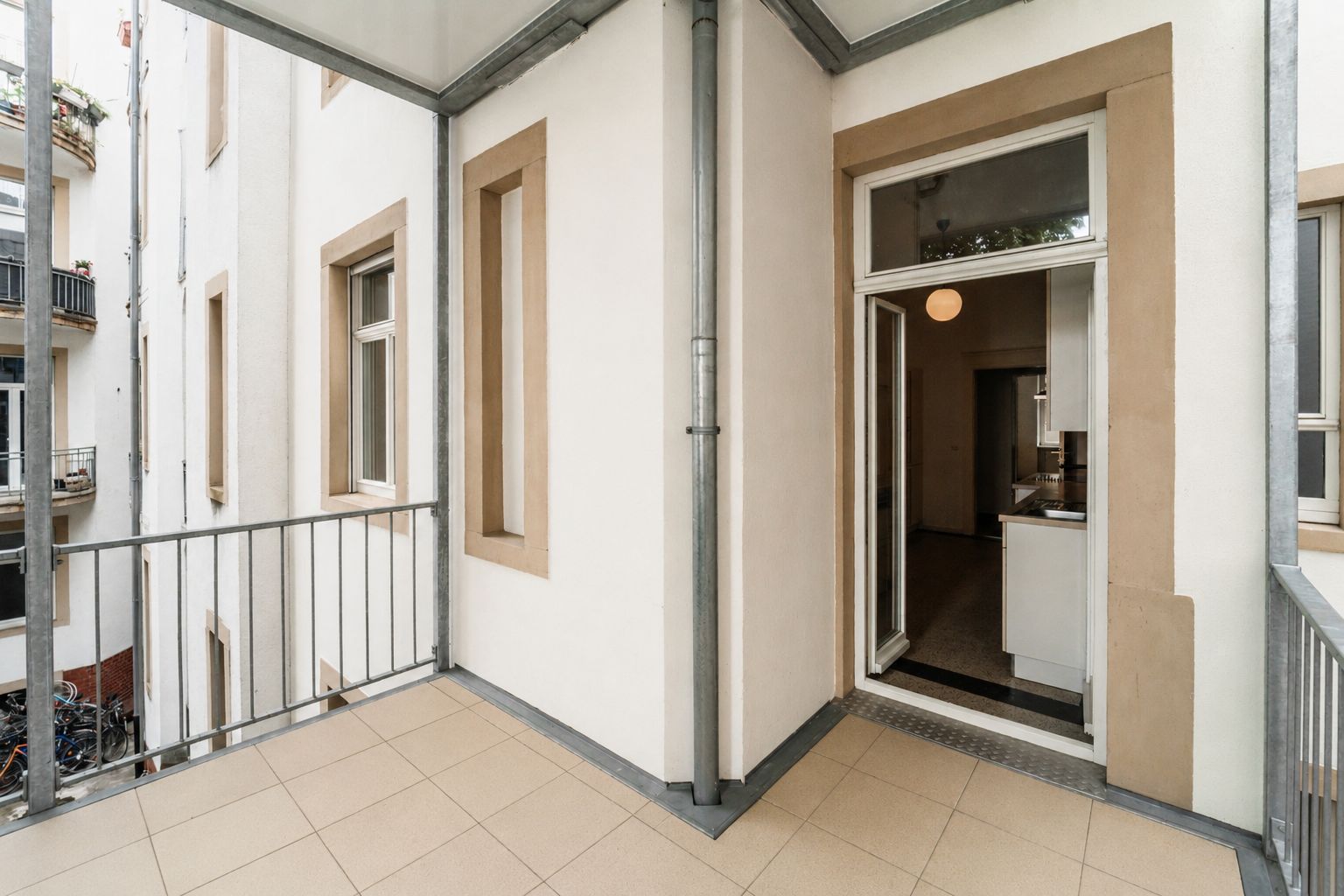 Überdachter Balkon mit Fliesenboden und Zugang zur Wohnung durch eine Glastür.