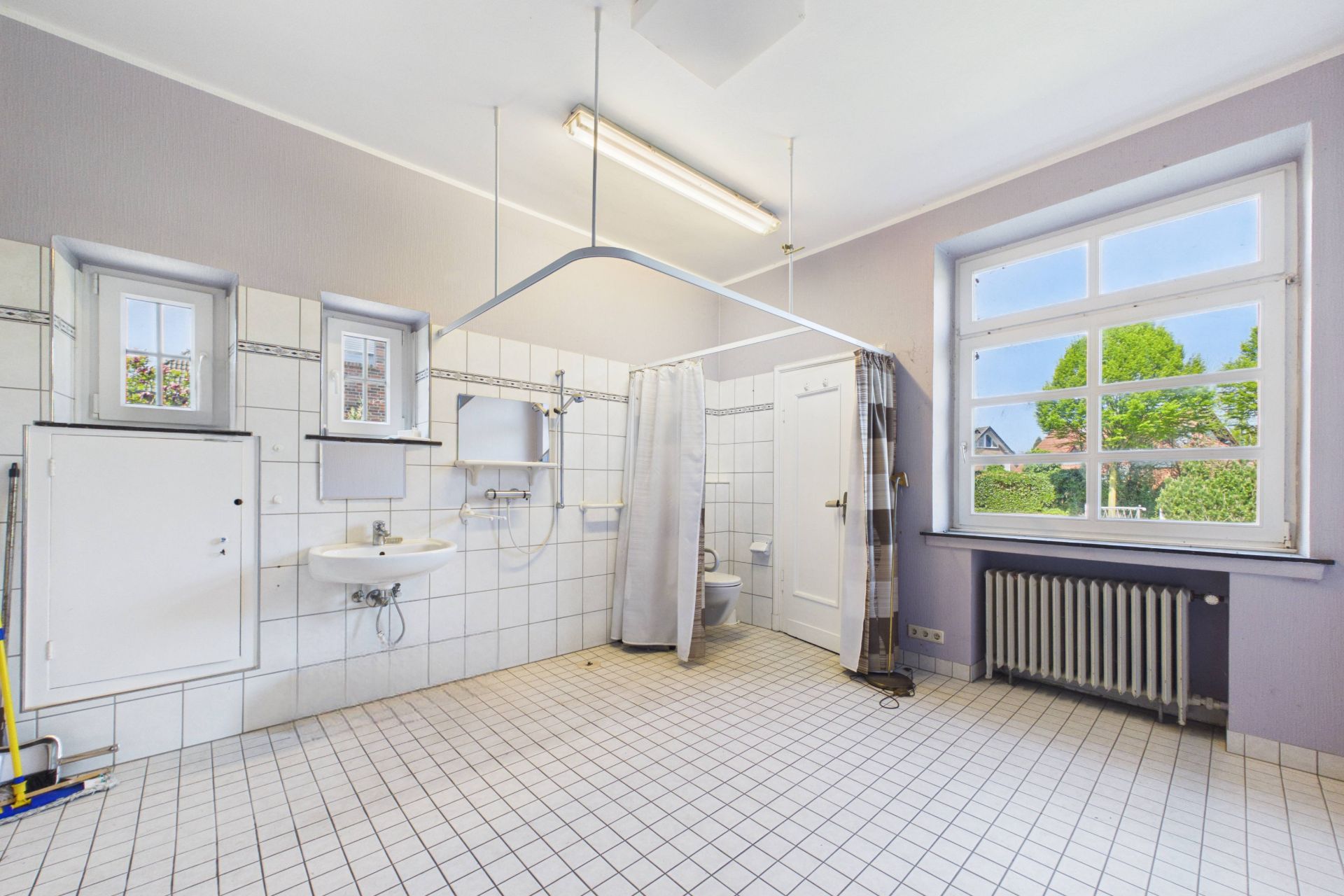 Großes, helles Badezimmer mit Kacheln, Waschbecken, Dusche mit Vorhang und Fenster.