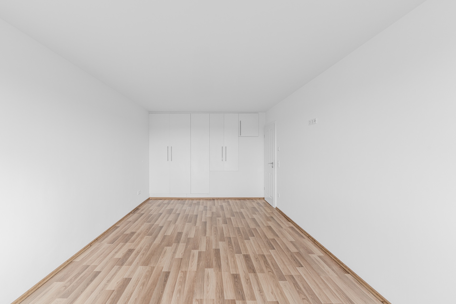 Leerer Raum mit hellem Holzboden, weißen Wänden und Einbauschrank.